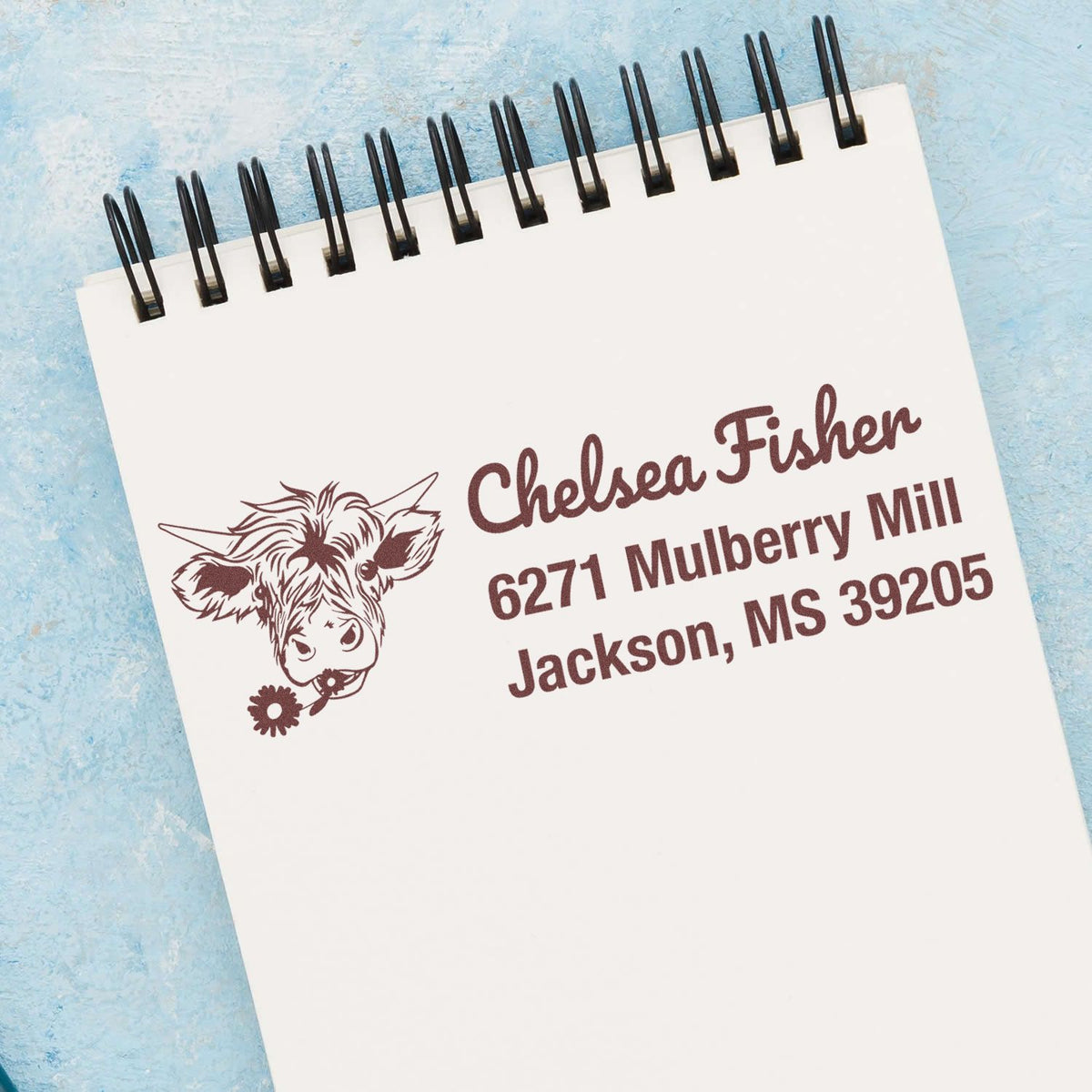 Custom cow return address rubber stamp with name and Jackson, MS mailing address on a spiral notebook.