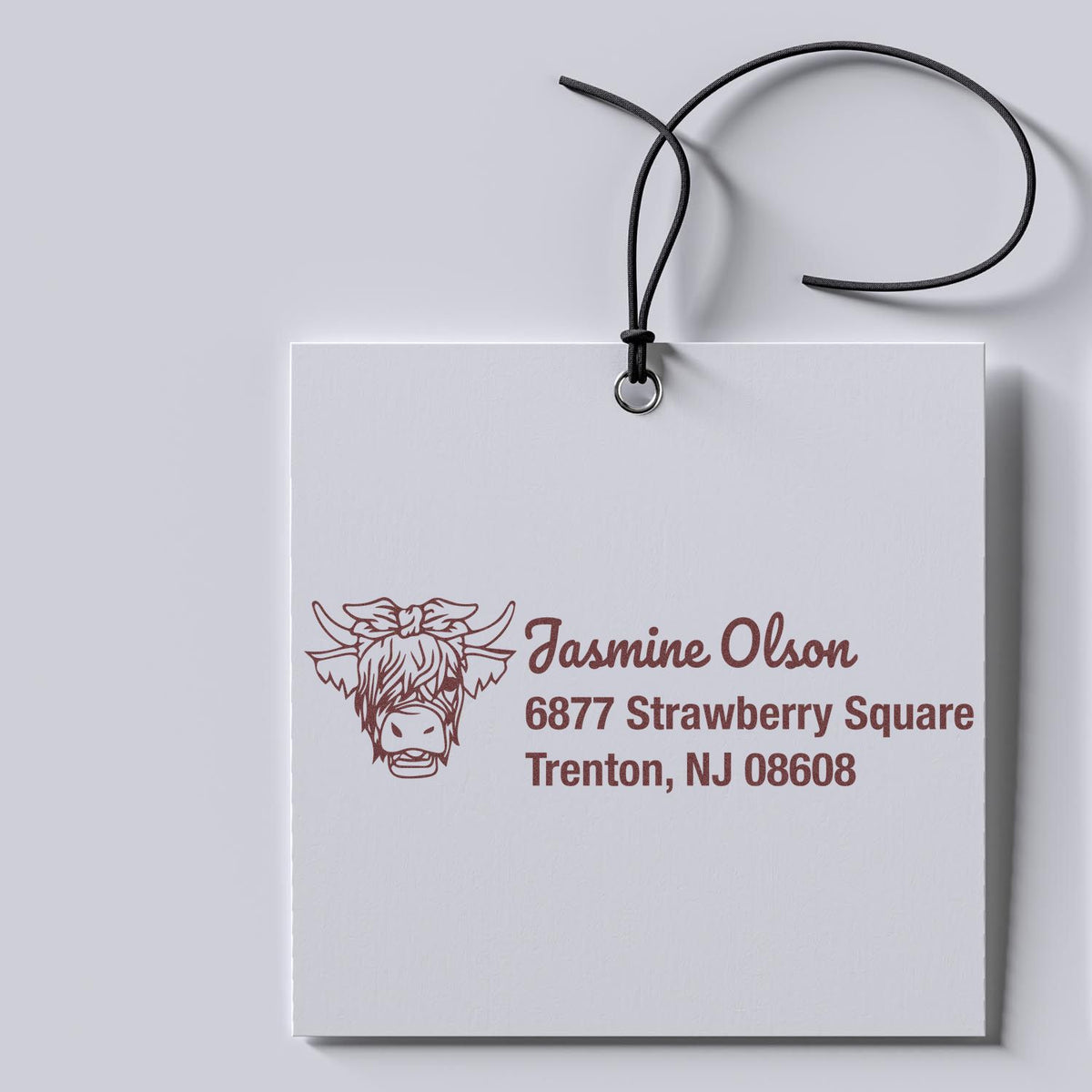 Custom return address rubber stamp with cow logo and name, shown on a hanging tag mockup.