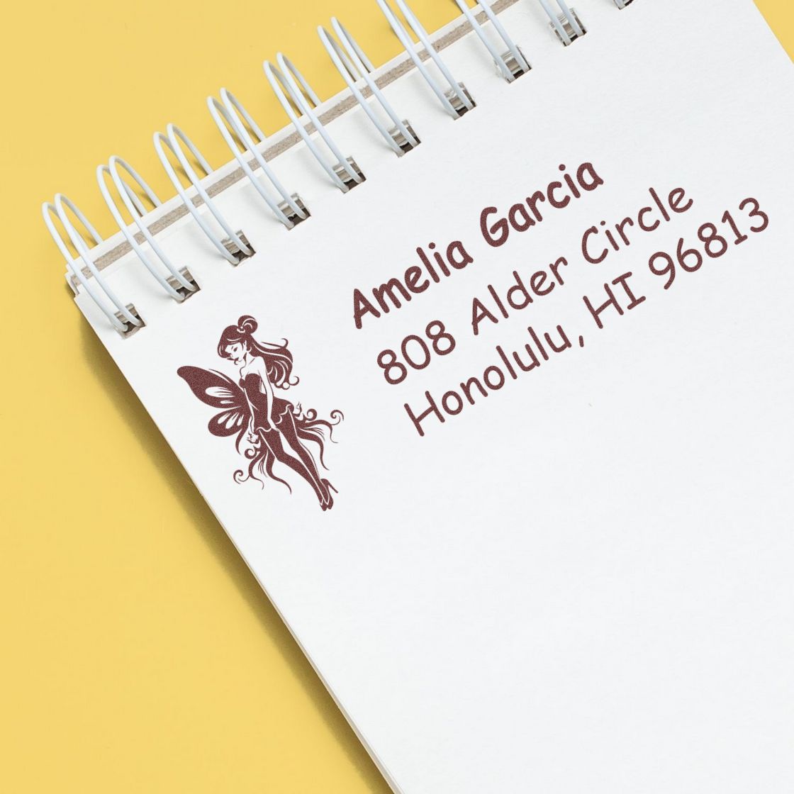 Custom rubber address stamp with fairy design and personalized name and Honolulu, HI address on a spiral notebook.