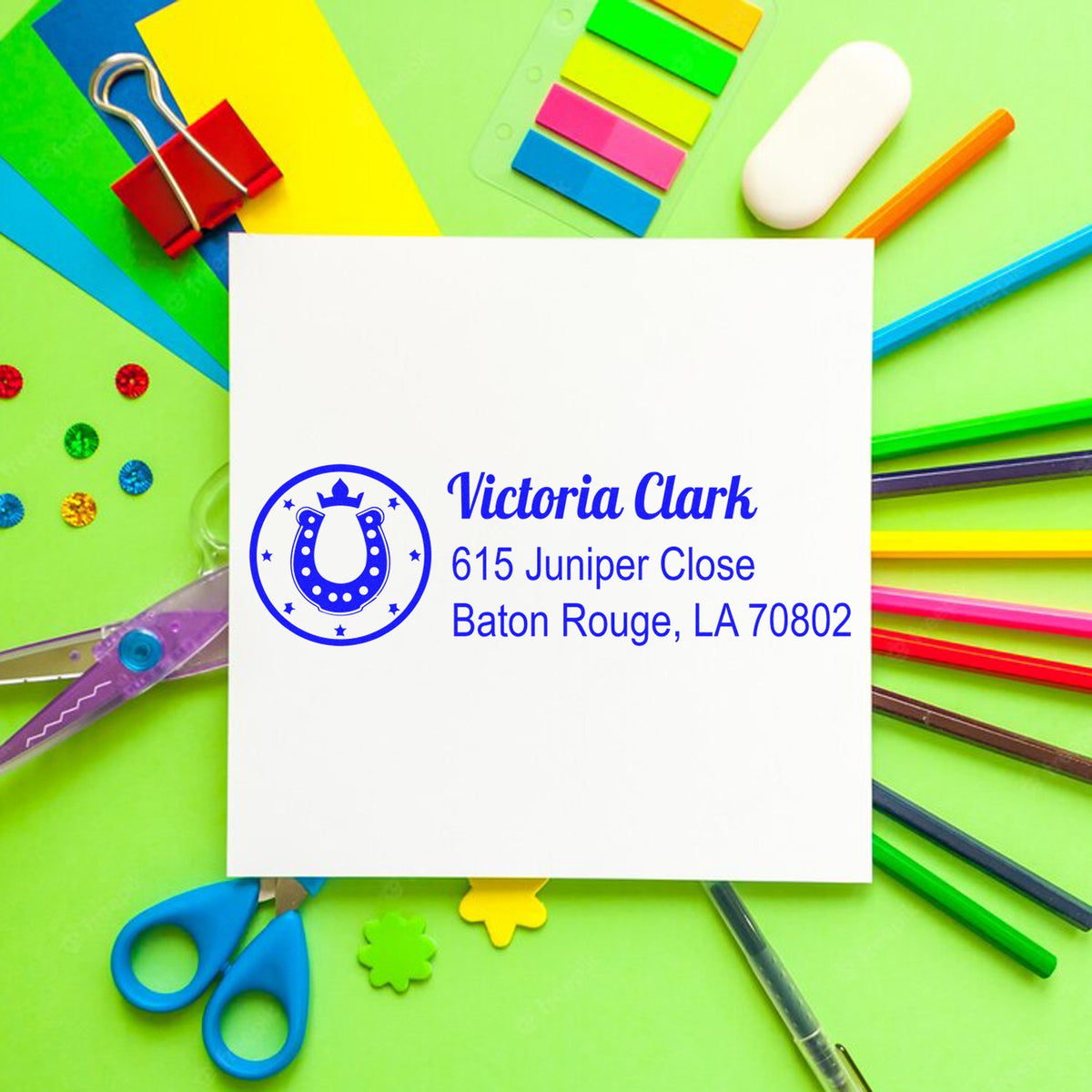 Custom address rubber stamp with horseshoe monogram for Victoria Clark, featuring name and Baton Rouge address on a colorful desk.