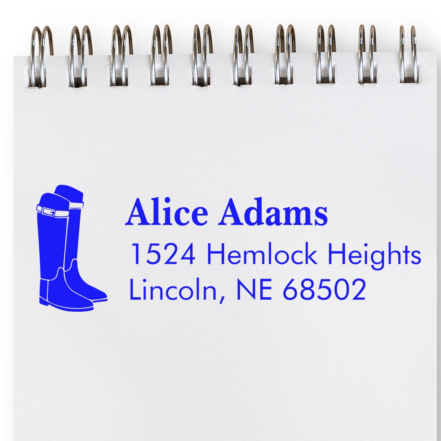 Custom address rubber stamp with boots icon for Alice Adams, 1524 Hemlock Heights, Lincoln, NE 68502 on a spiral notebook page.