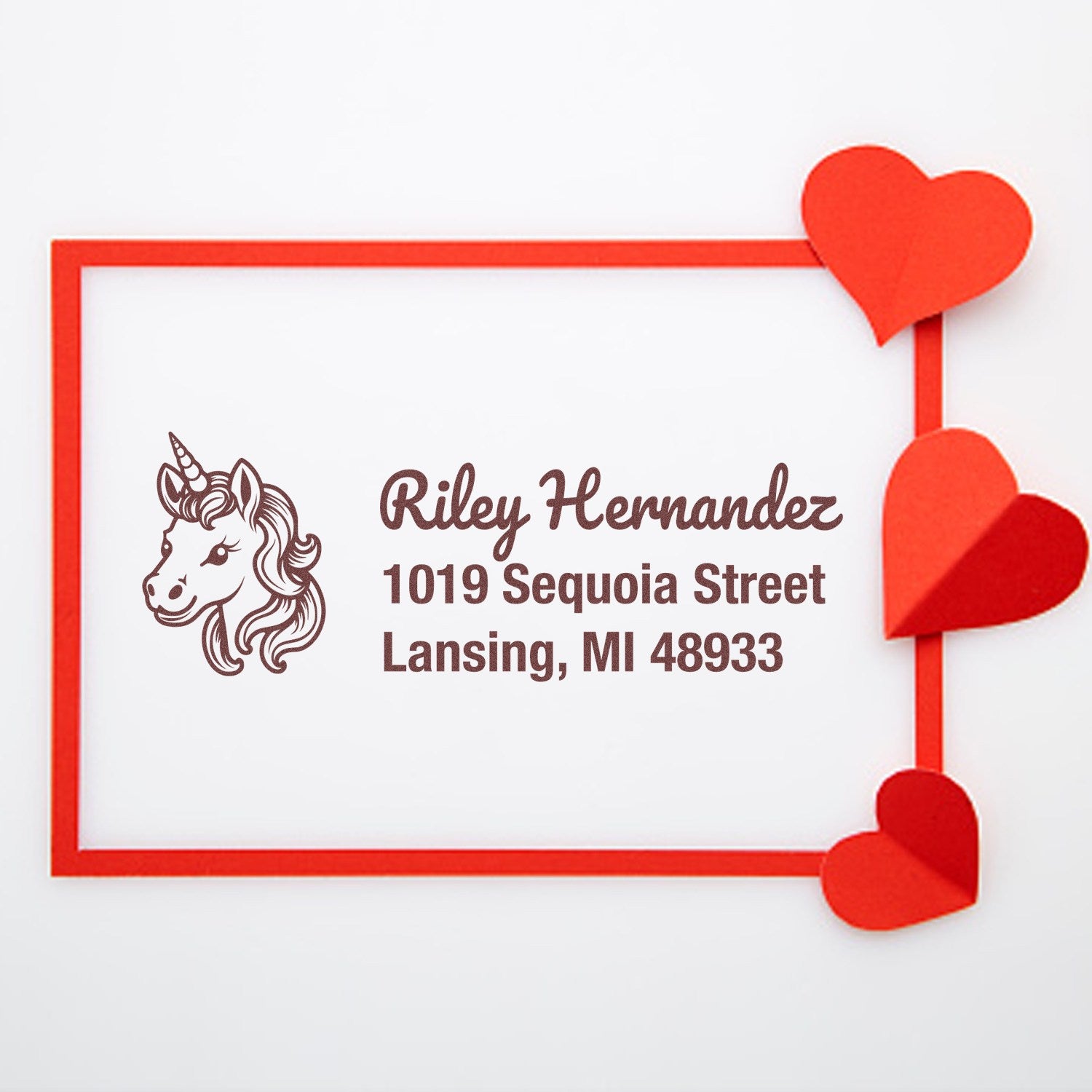 Custom unicorn address rubber stamp design with name Riley Hernandez and Lansing, MI 48933, framed by red hearts.