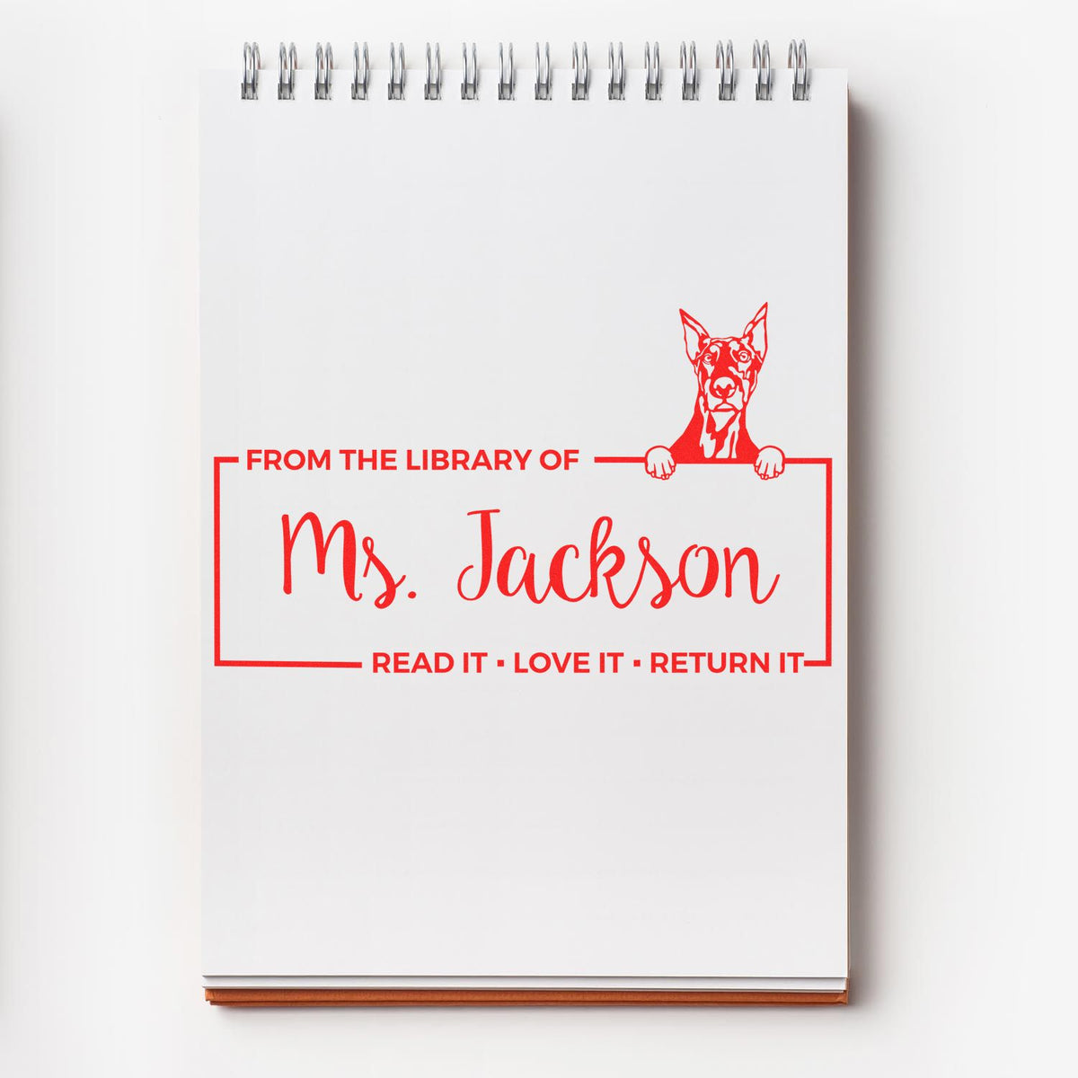 Custom library rubber stamp on notebook reading From the Library of Ms. JacksonRead it, Love it, Return it with dog design.