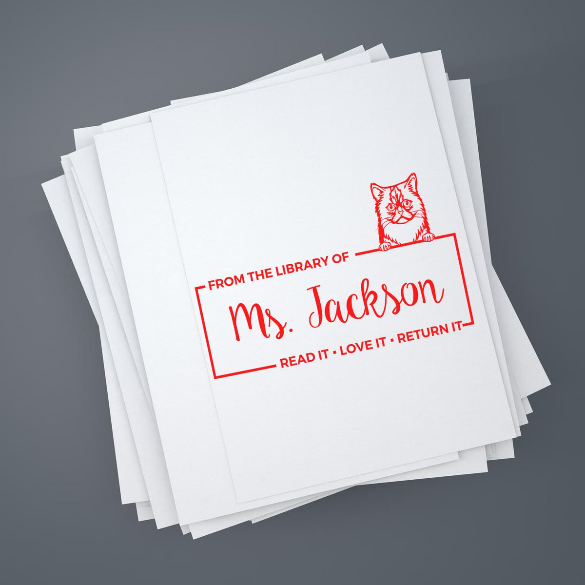 Personalized library rubber stamp for books, featuring cat design and Ms. Jackson name, on stacked papers.