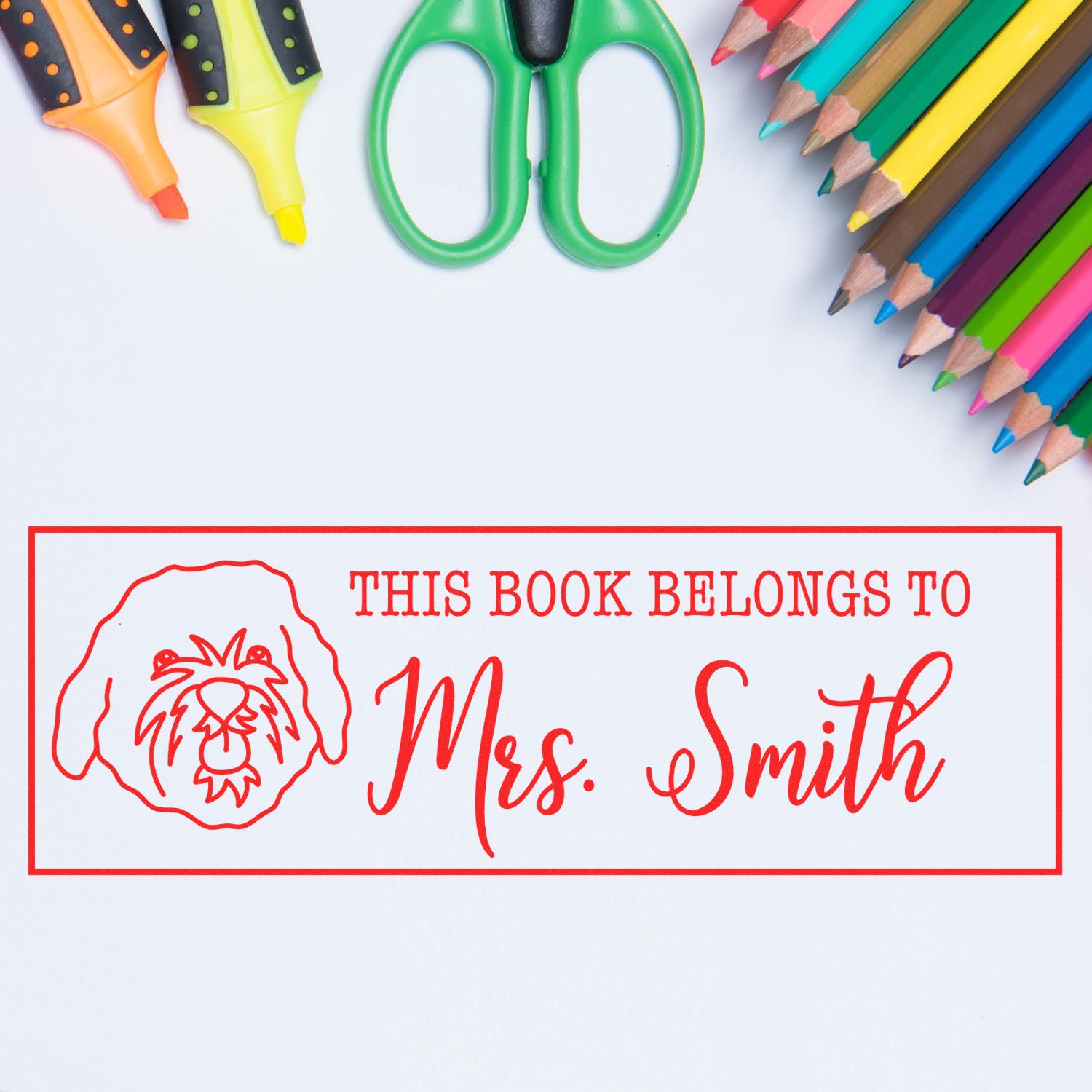 Custom rubber stamp bookplate reading This Book Belongs to Mrs. Smith with lion logo and school supplies.