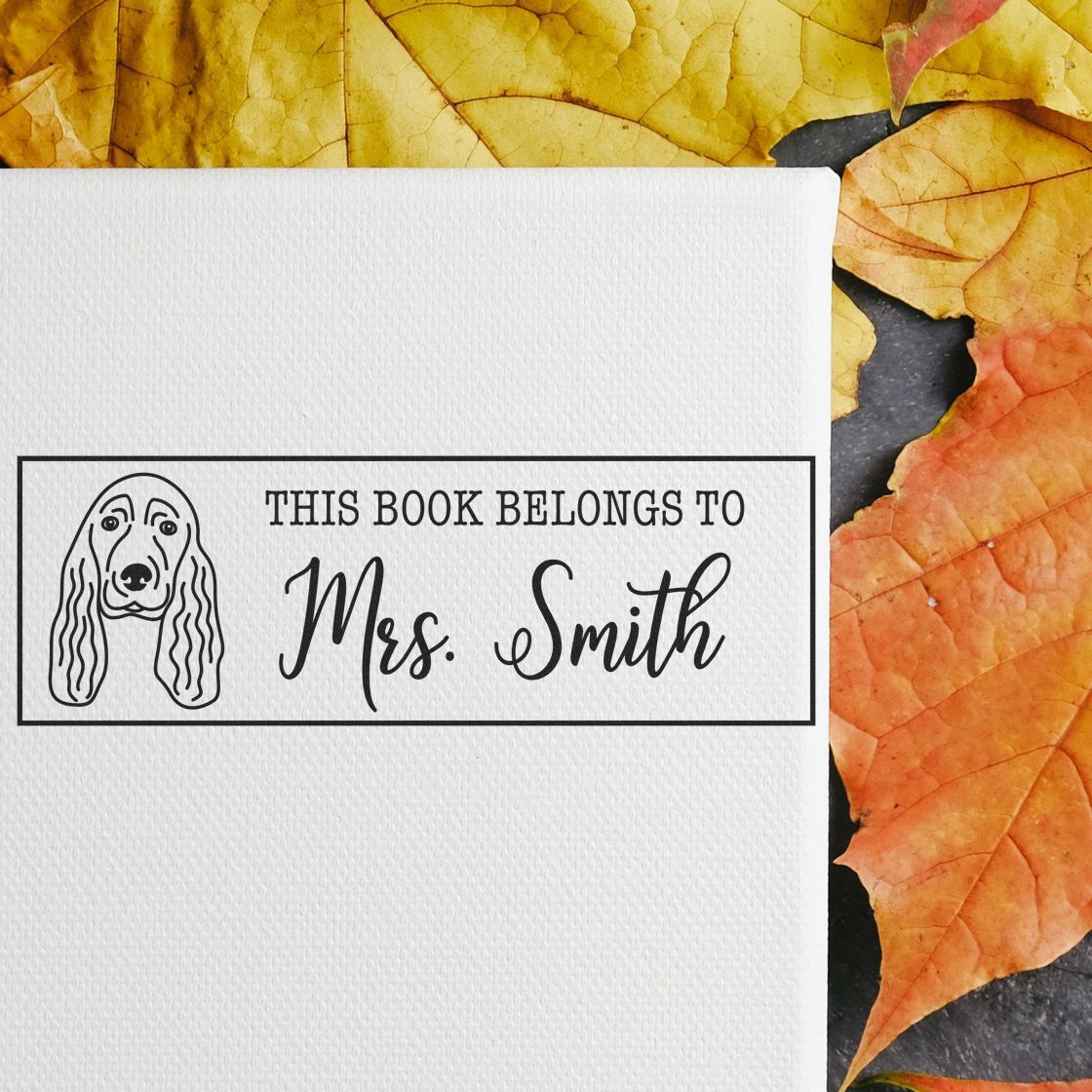 Custom rubber book stamp with dog illustration and This Book Belongs to Mrs. Smith text for personalized library labeling.