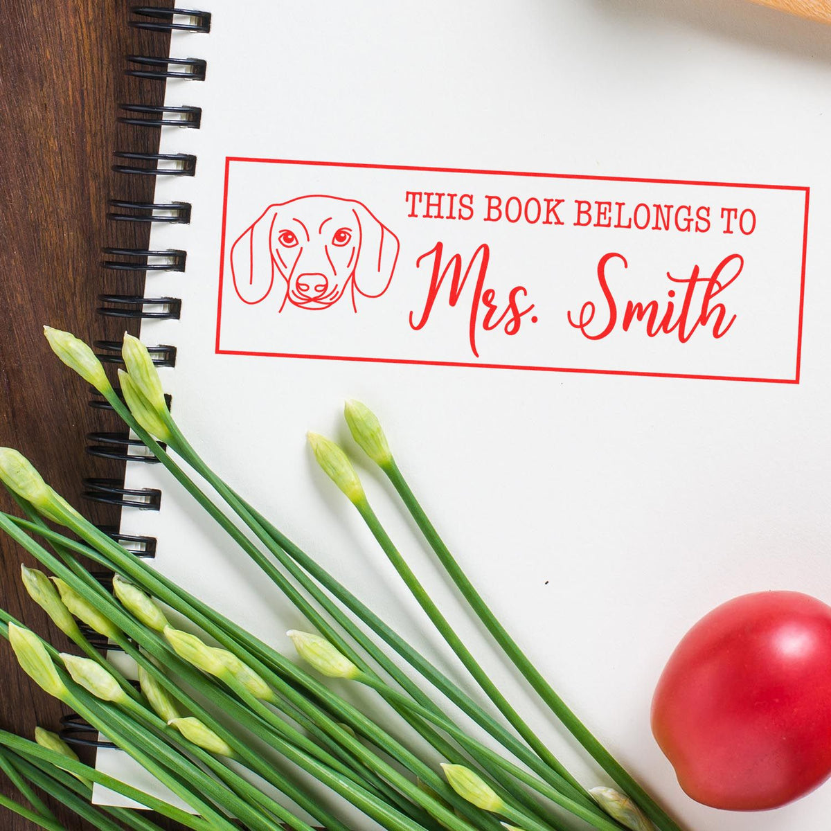 Personalized rubber book stamp with dog icon, featuring This Book Belongs to Mrs. Smith ex libris design on a notebook.