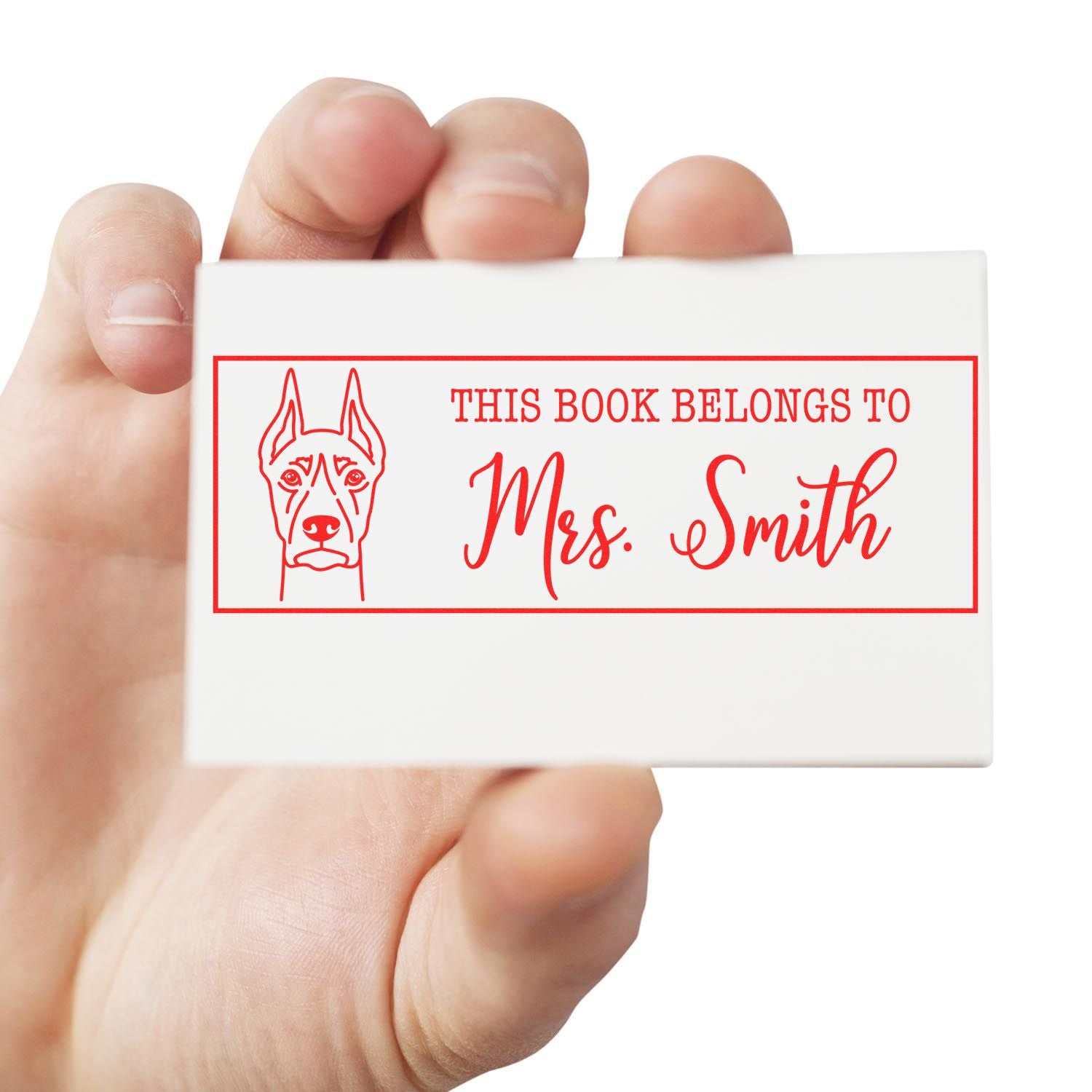 Custom dog rubber book stamp reading This Book Belongs to Mrs. Smith, held in hand for personal library labeling.