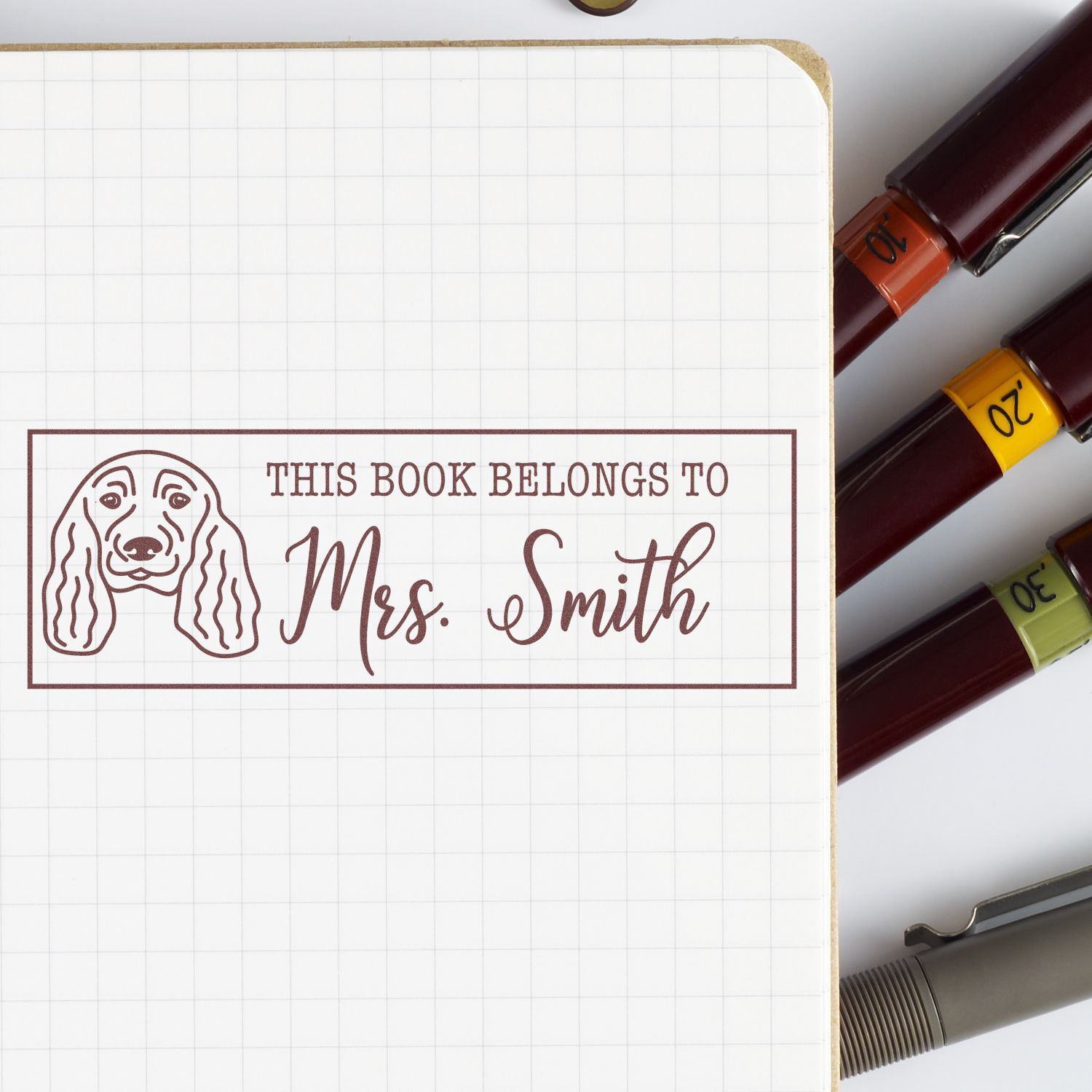 Personalized dog book rubber stamp reading This Book Belongs to Mrs. Smith on notebook paper.