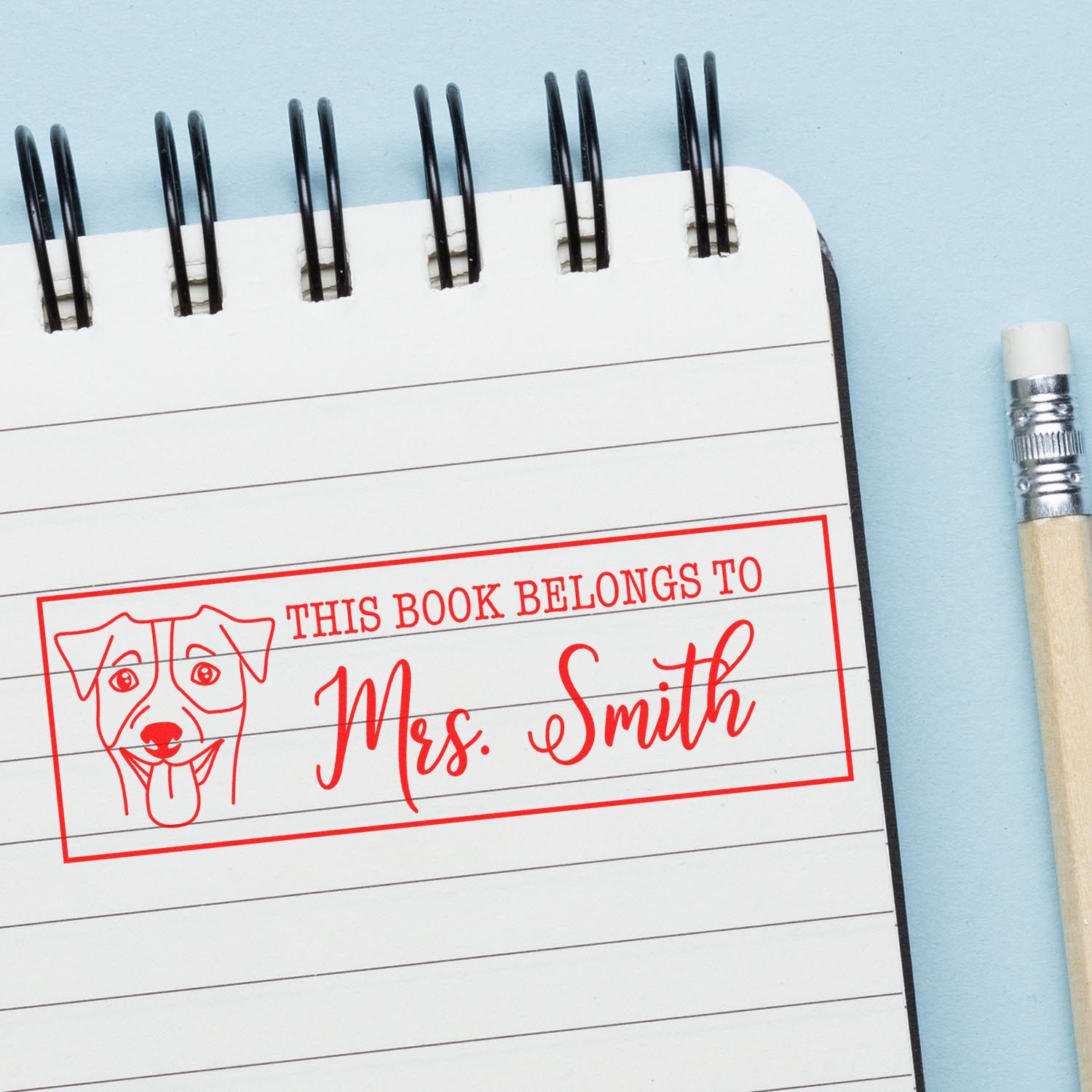 Personalized rubber stamp imprint reading This book belongs to Mrs. Smith with dog icon on a notebook page.