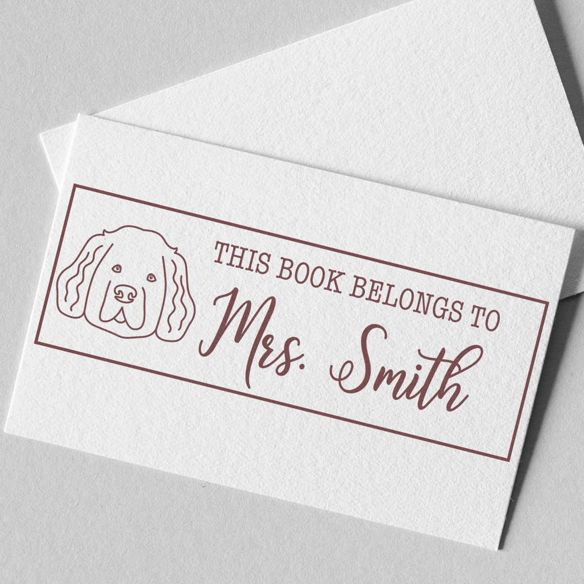 Personalized rubber book stamp with dog illustration and This Book Belongs to Mrs. Smith for custom bookplates.