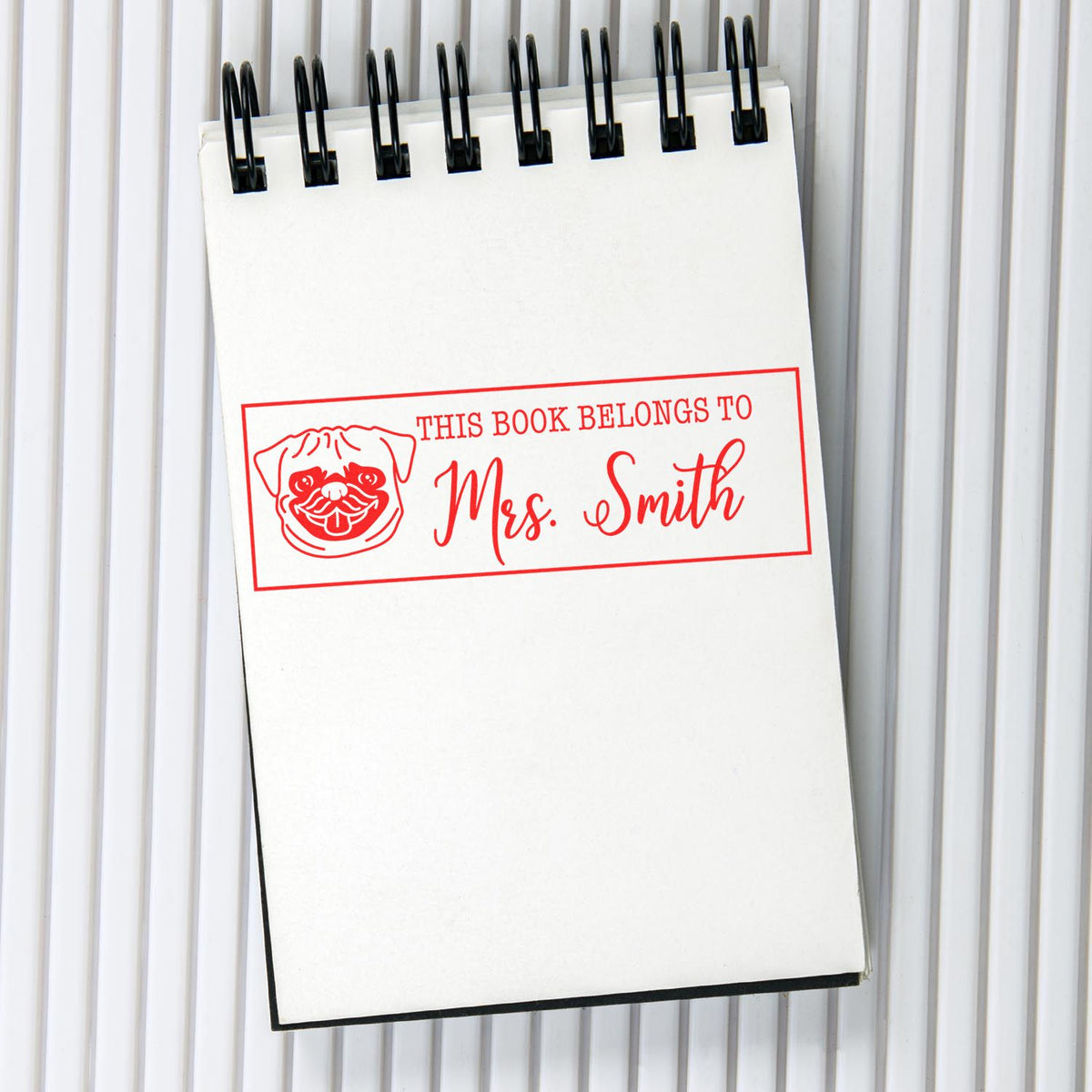 Personalized rubber book stamp with pug design reading This Book Belongs to Mrs. Smith for library ownership.