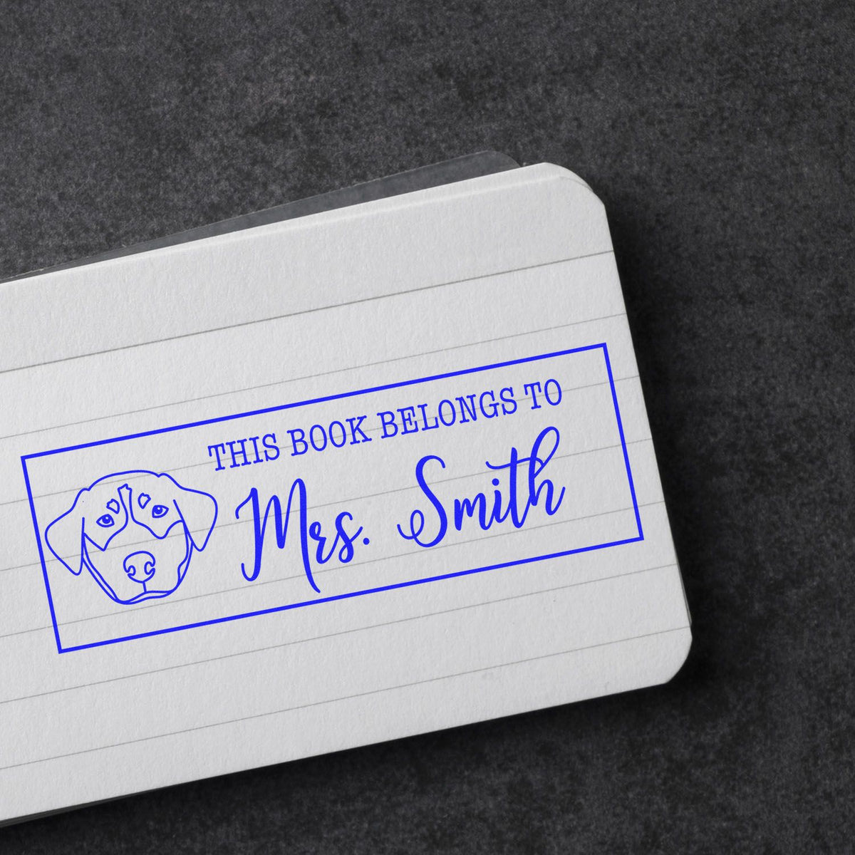 Personalized rubber book stamp with dog design reading This Book Belongs to Mrs. Smith for library books.