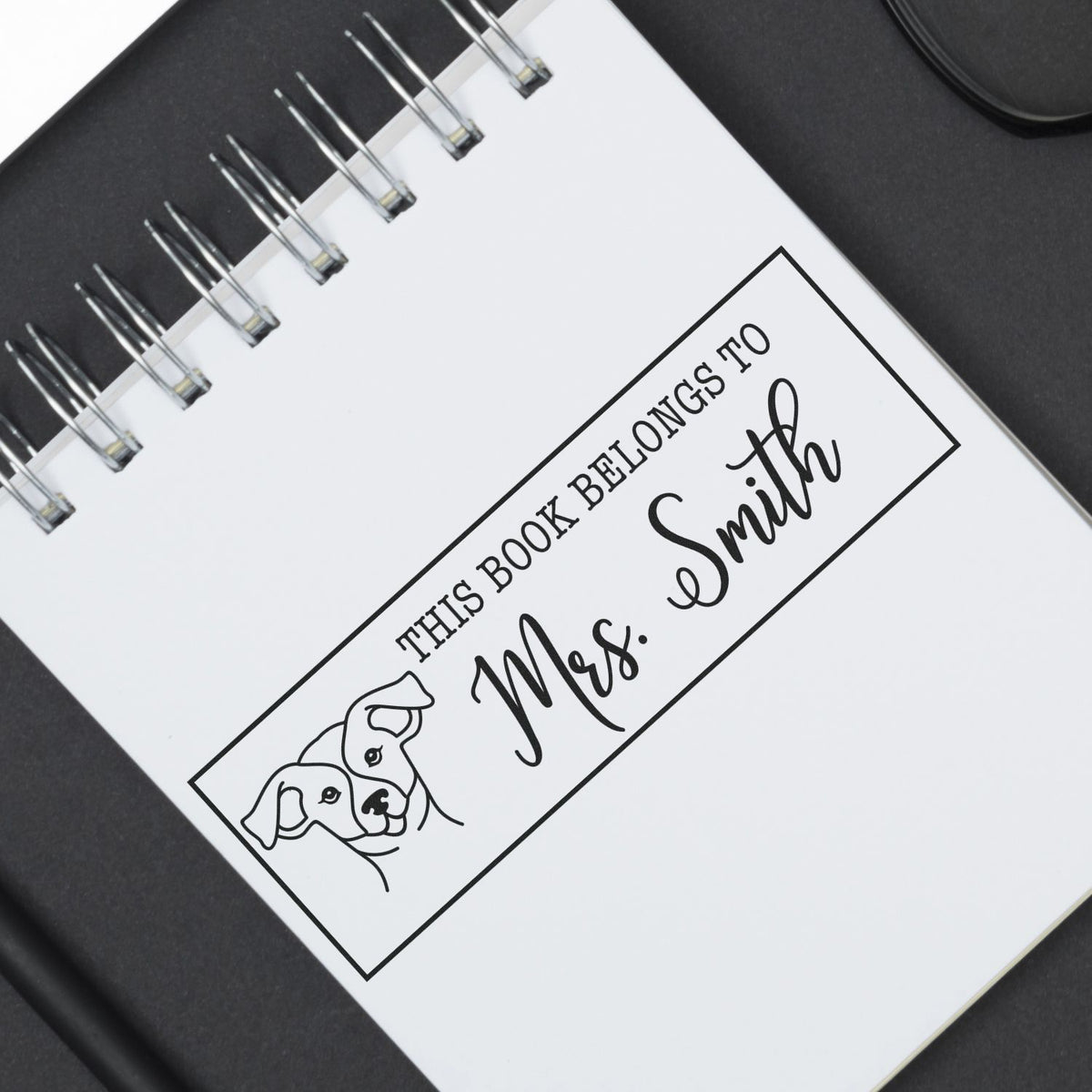 Custom rubber book stamp design reading This Book Belongs to Mrs. Smith with dog illustration for personalized library marking.