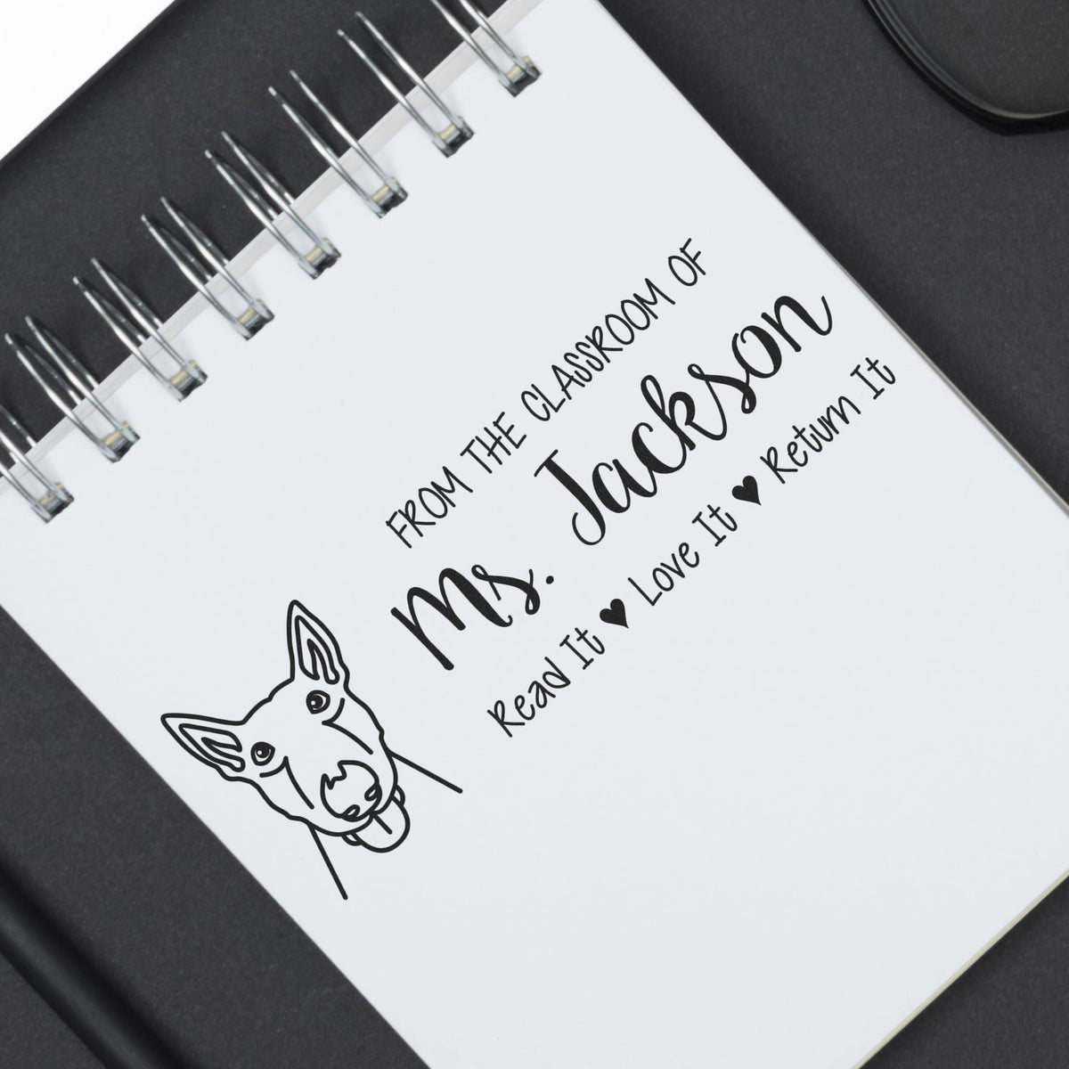 Custom teacher rubber stamp on notebook page reading From the classroom of Mr. JacksonRead it, Love it, Return it with dog icon.