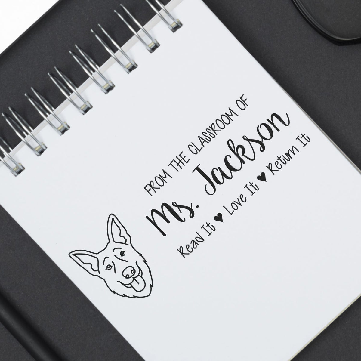 Custom teacher rubber stamp with dog illustration and personalized From the classroom of Mrs. Jackson design on a notebook.
