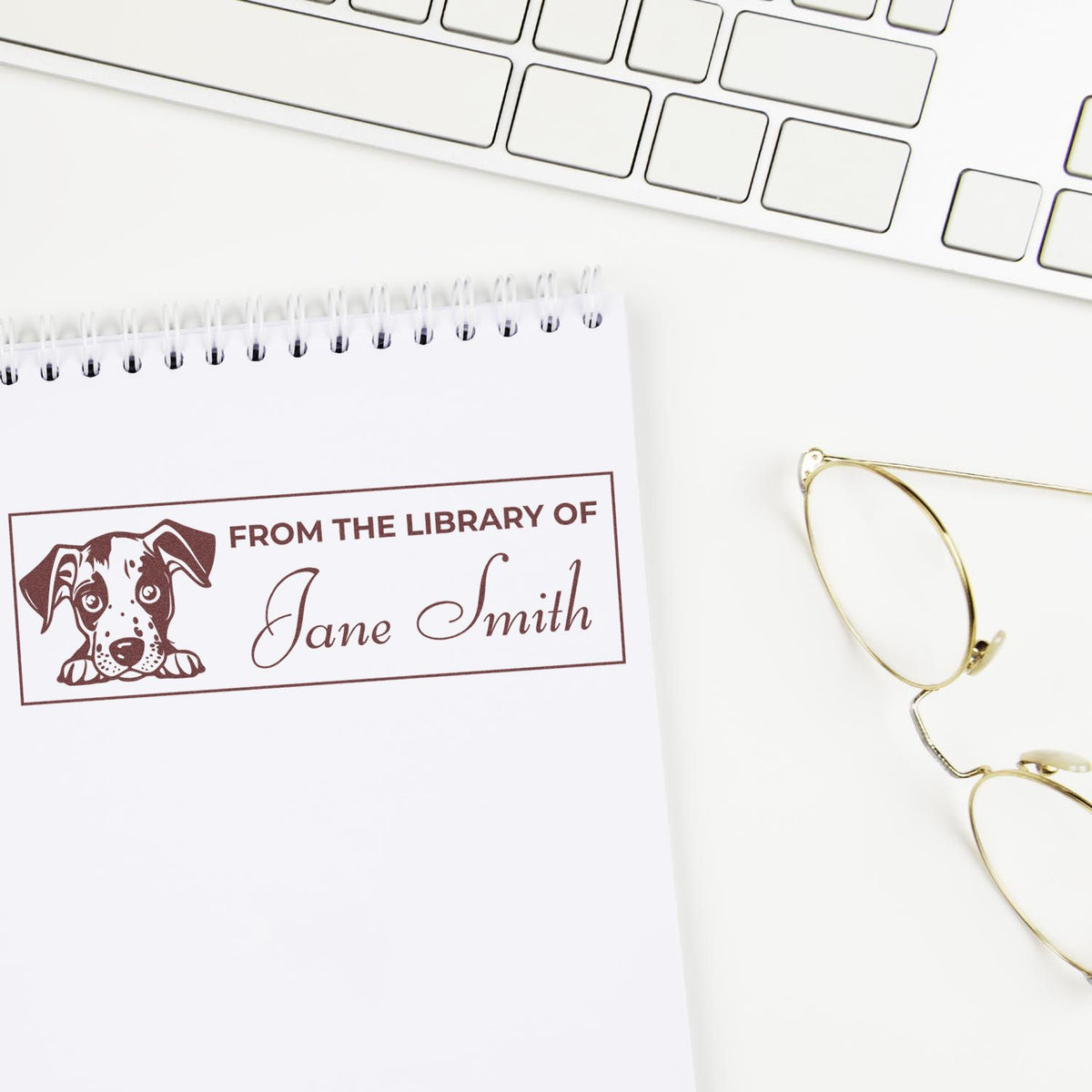 Personalized rubber stamp for books with dog design reading From the Library of Jane Smith on a notebook.