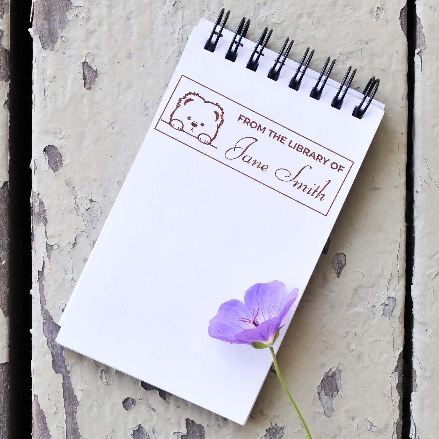 Personalized book rubber stamp with bear design reading From the library of Jane Smith on a notebook.