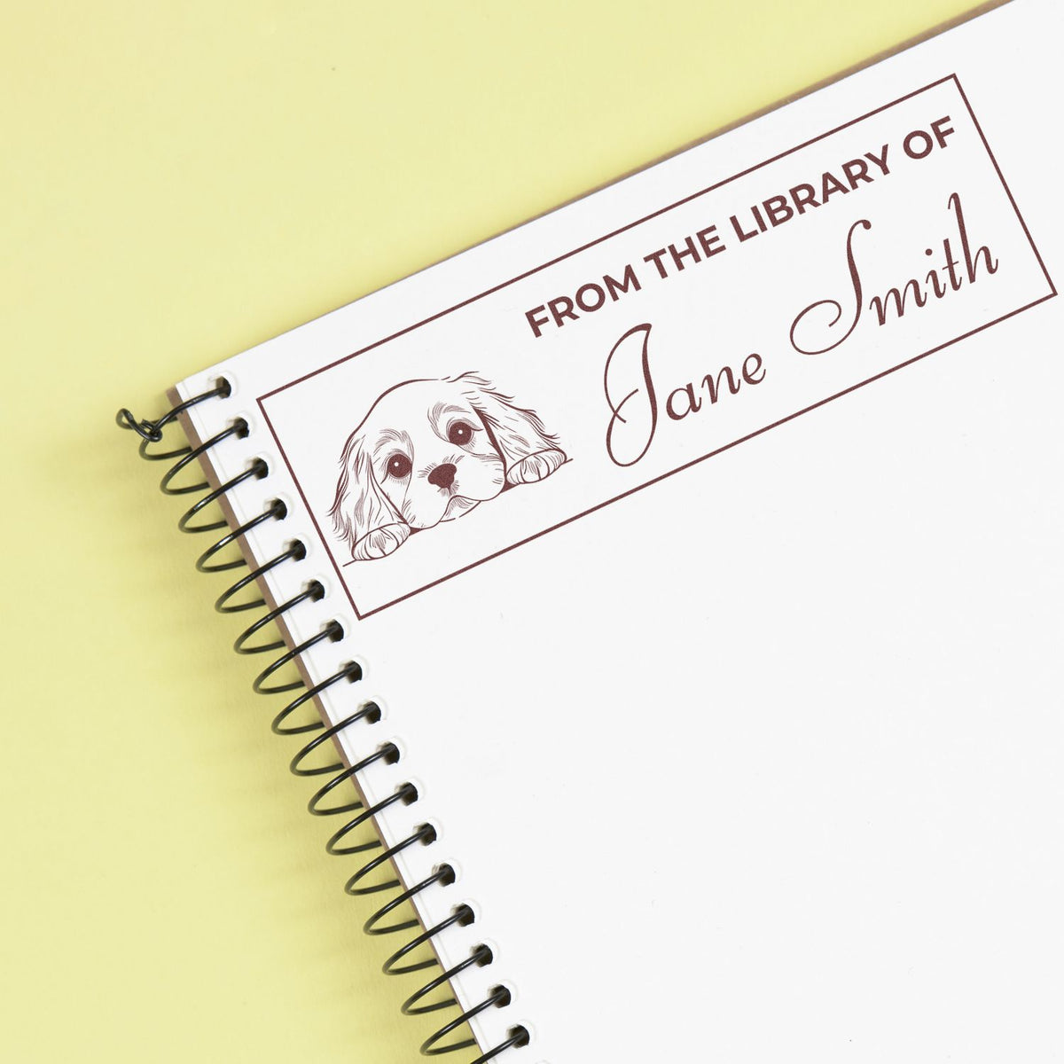 Custom rubber library stamp with dog illustration and From the Library of Jane Smith on a spiral notebook.