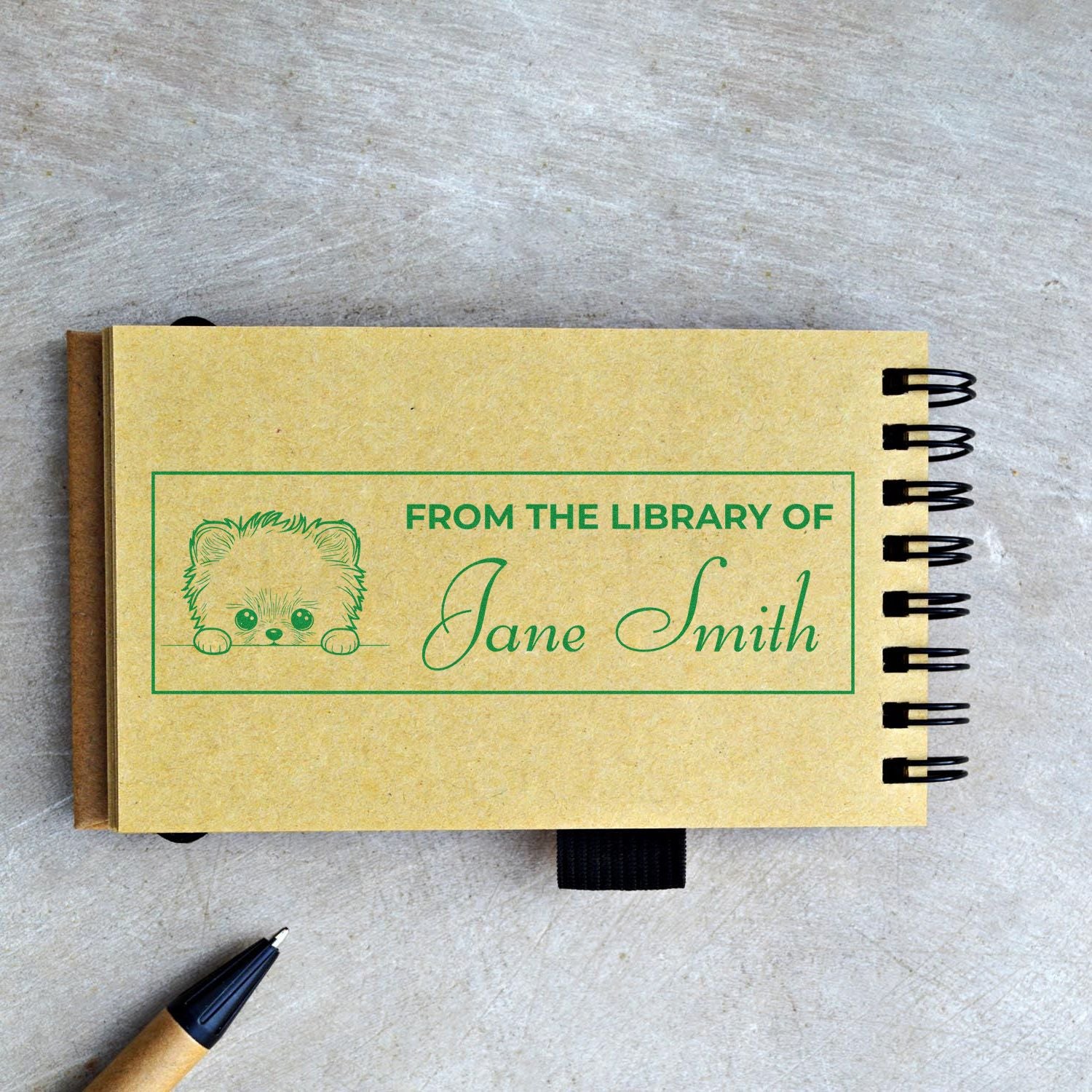 Personalized book stamp reading From the Library of Jane Smith with cute bear design on a spiral notebook.