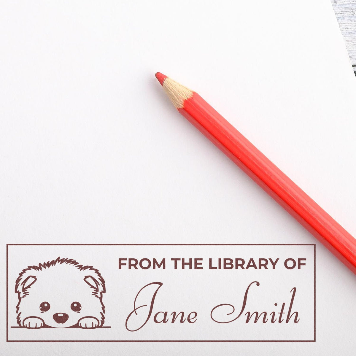 Personalized rubber library stamp with puppy design and From the Library of Jane Smith imprint beside a red pencil.