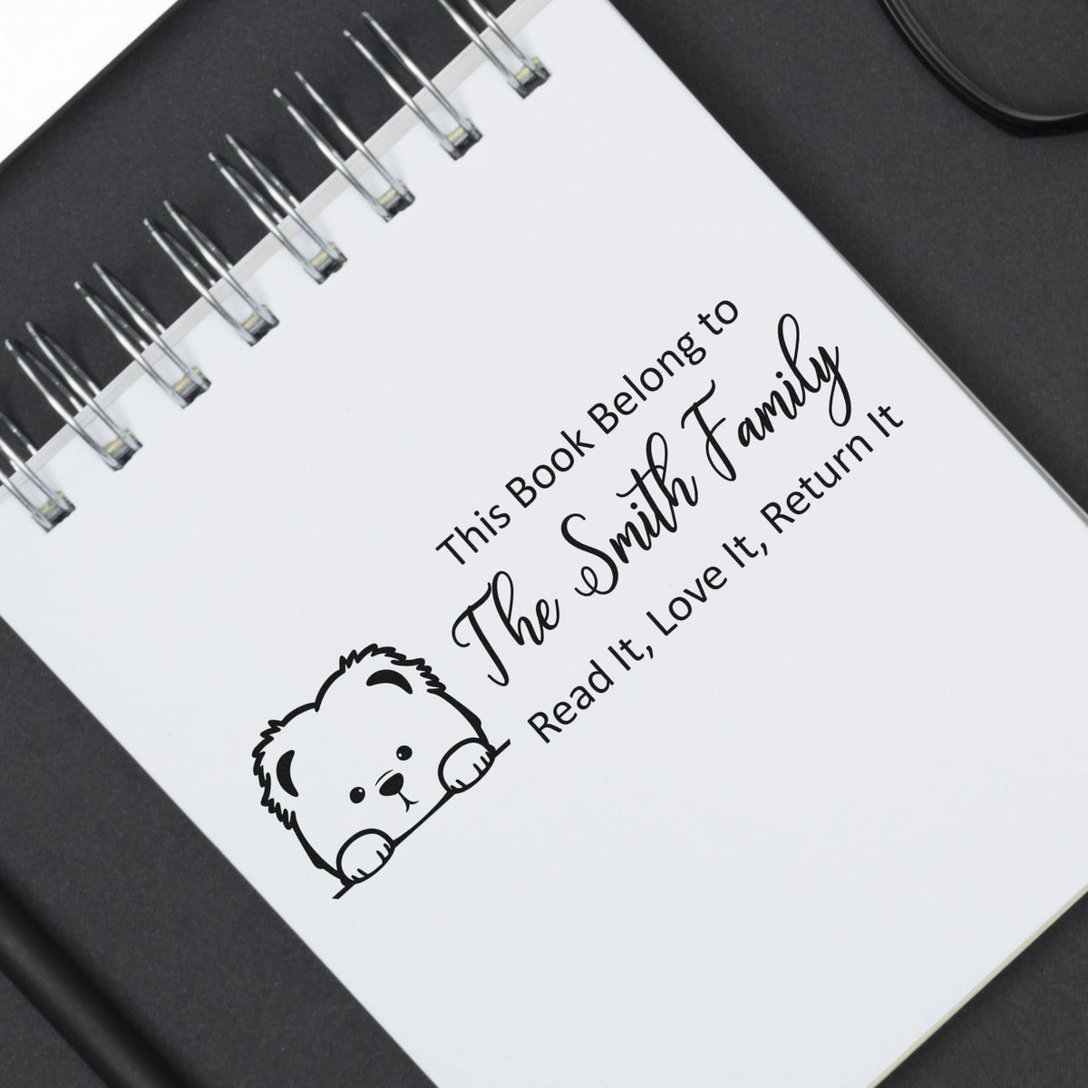 Personalized rubber book stamp with teddy bear, marking a family library book: This Book Belong to The Smith Family, Read It, Love It, Return It.