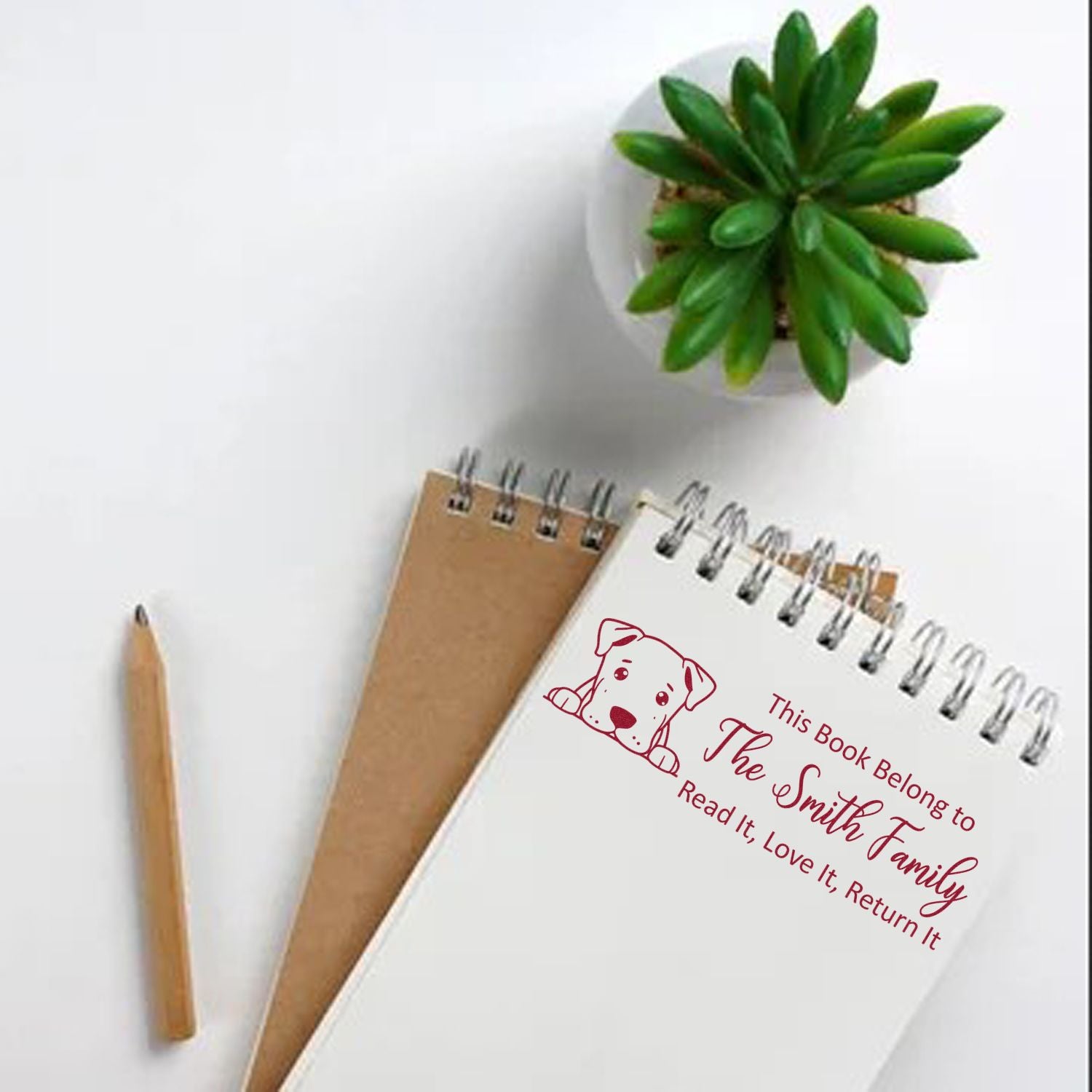 Personalized rubber book stamp on notebook, with dog icon and This Book Belongs to The Smith Family return-it message.