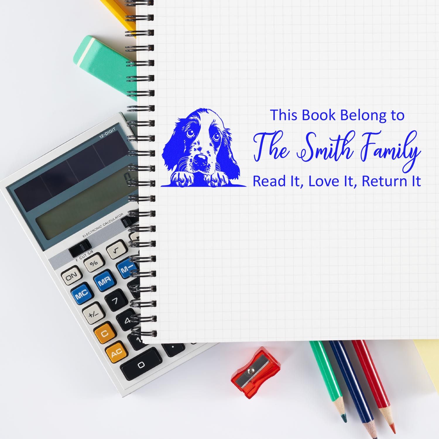 Personalized rubber book stamp with dog design and This Book Belongs to The Smith Family return-to-owner message on notebook.