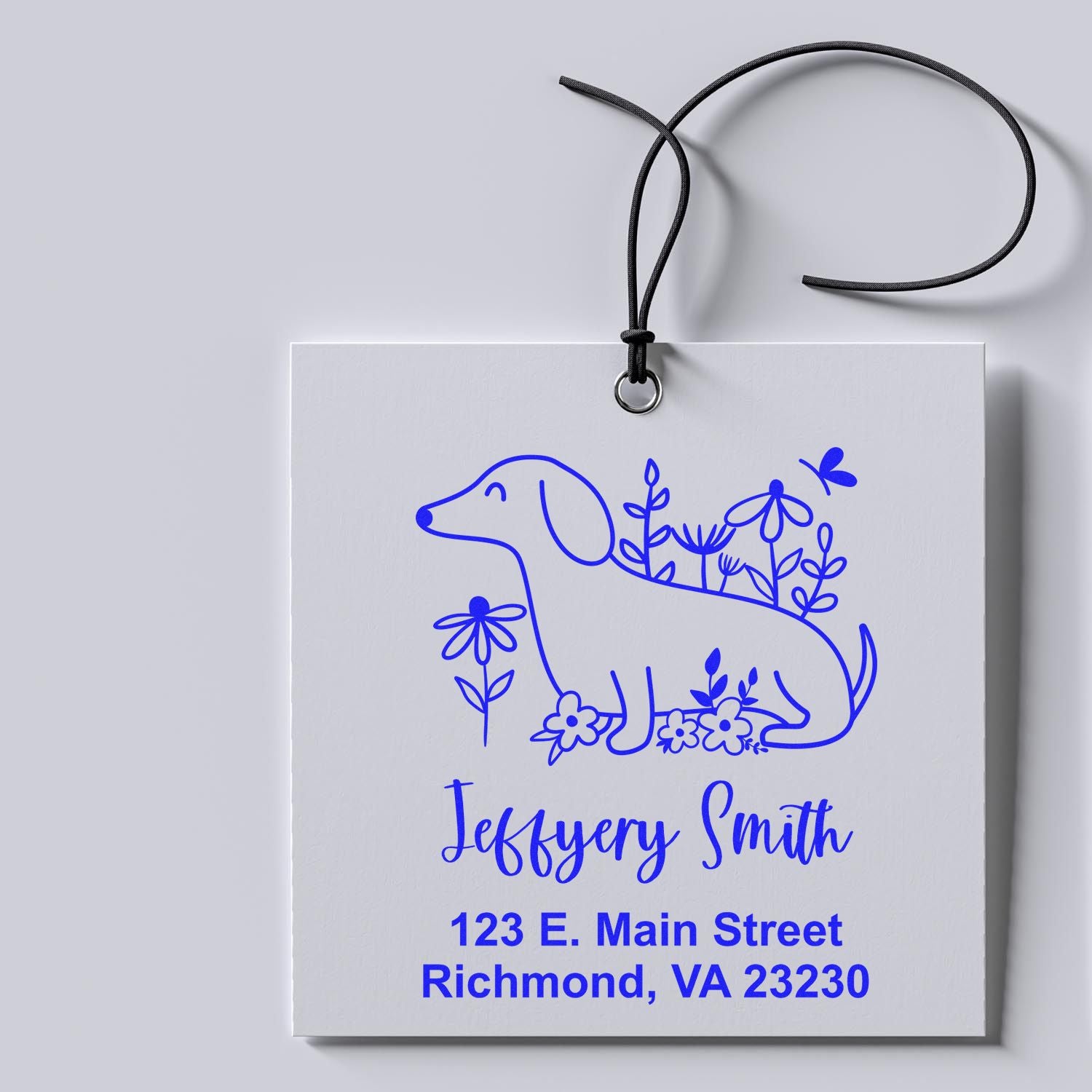 Custom rubber stamp with floral dog design, personalized name and address, shown on a hanging gift tag.