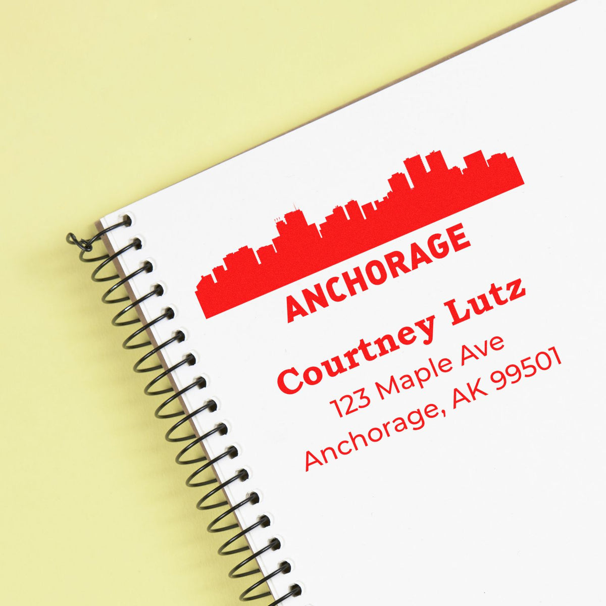Custom Anchorage rubber address stamp with skyline logo, Courtney Lutz name, and mailing address on a spiral notebook.