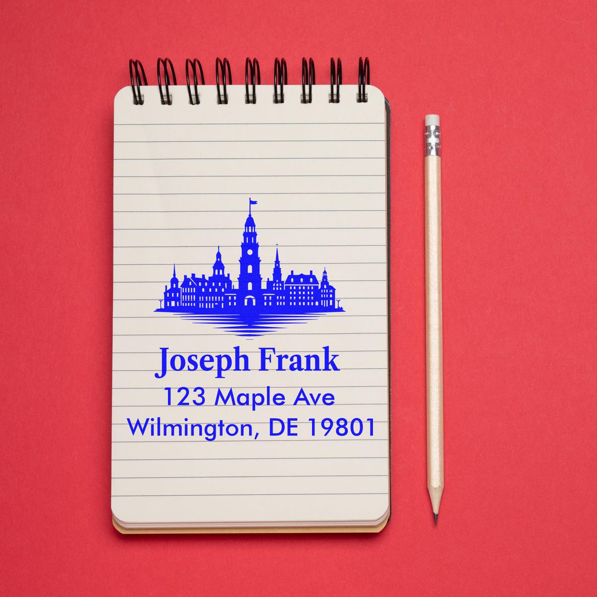 Custom address rubber stamp with city skyline design on a notebook, showing Joseph Frank, 123 Maple Ave, Wilmington, DE 19801.
