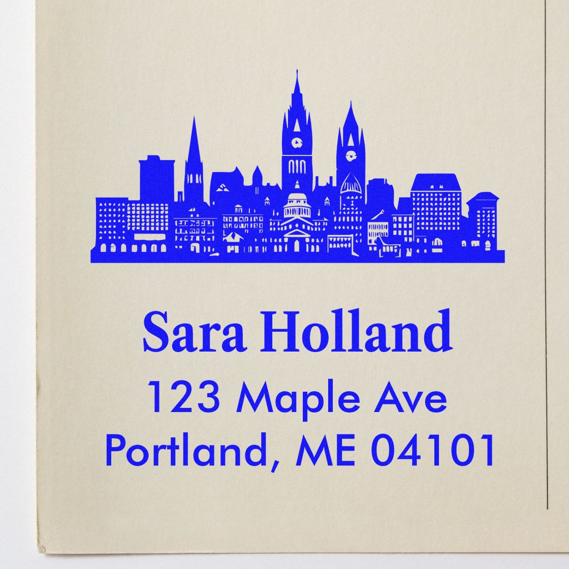 Custom rubber stamp with city skyline and return address for Sara Holland, 123 Maple Ave, Portland, ME 04101.