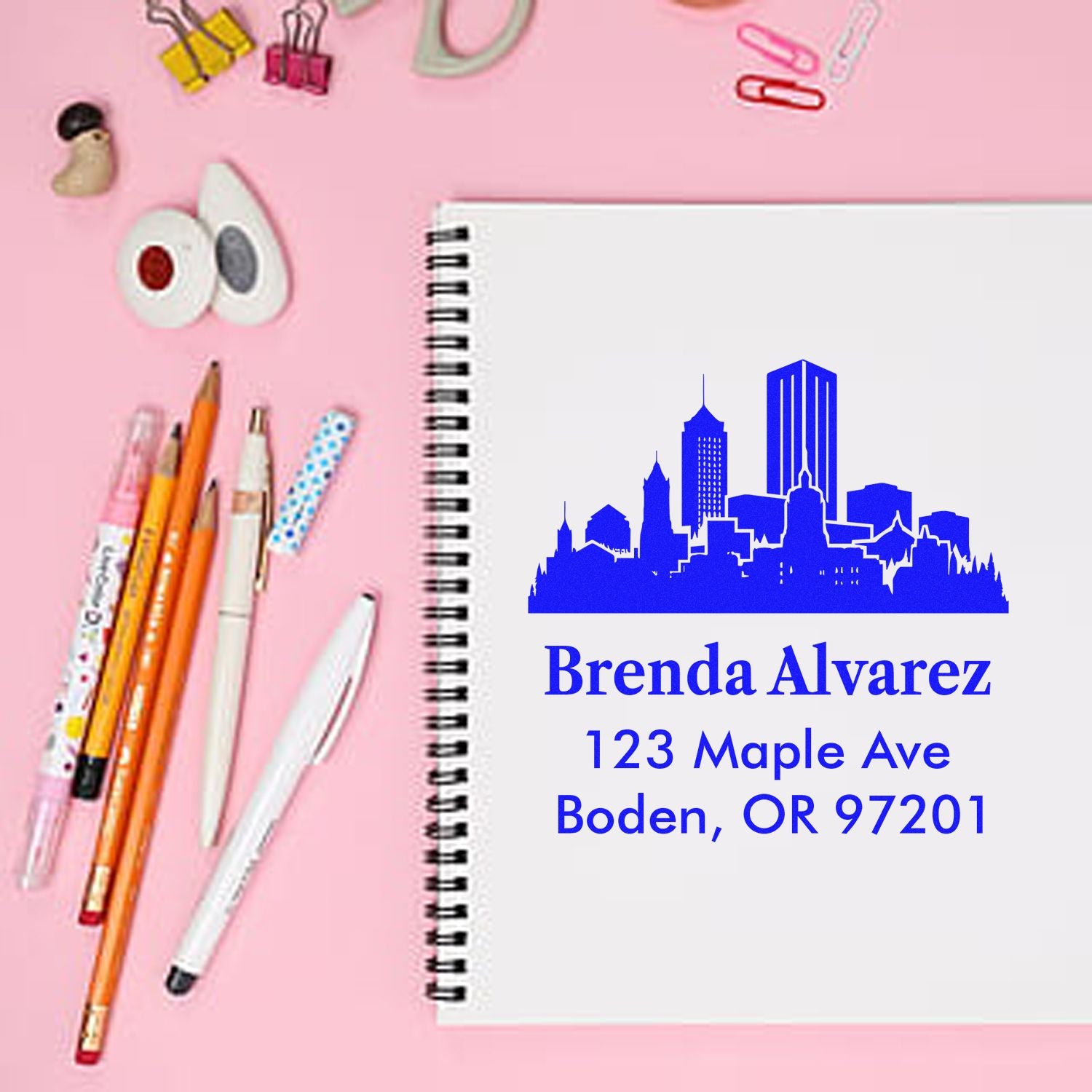 Custom rubber address stamp with skyline design on notebook, paired with pens for personalized stationery.