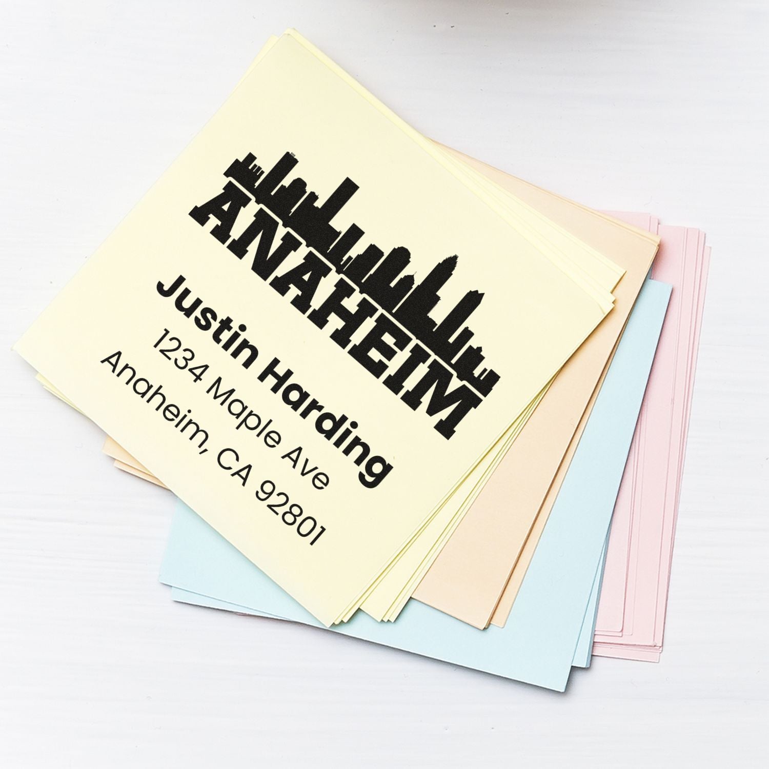 Custom rubber stamp for business stationery, showing logo, name, and Anaheim address on colored paper samples.
