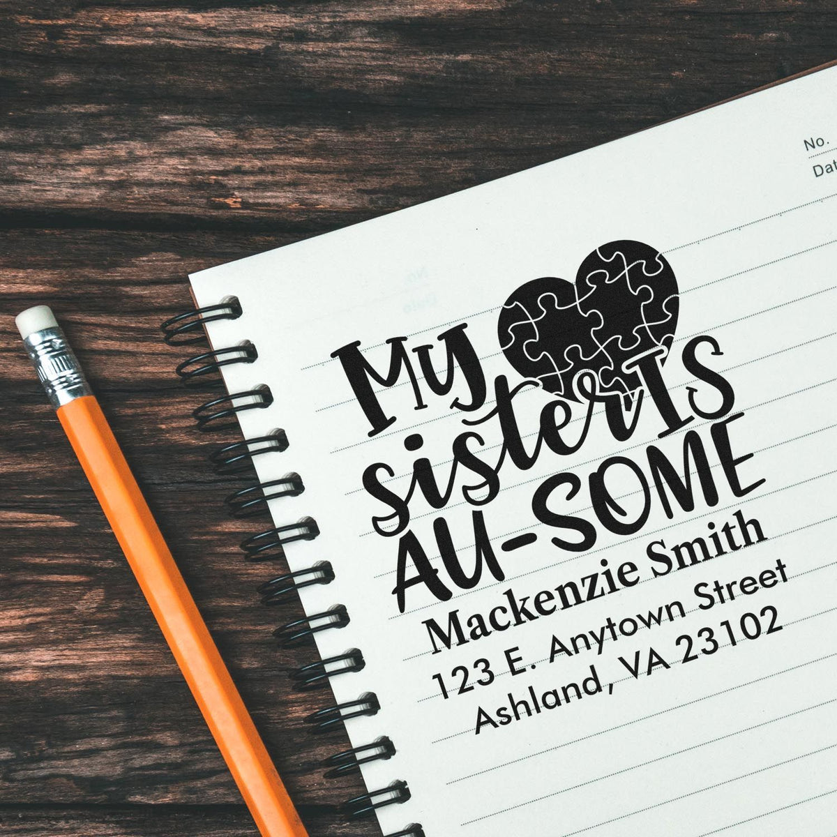 Custom rubber stamp for sisters with puzzle-heart design and personalized name and address, shown stamped in a notebook.