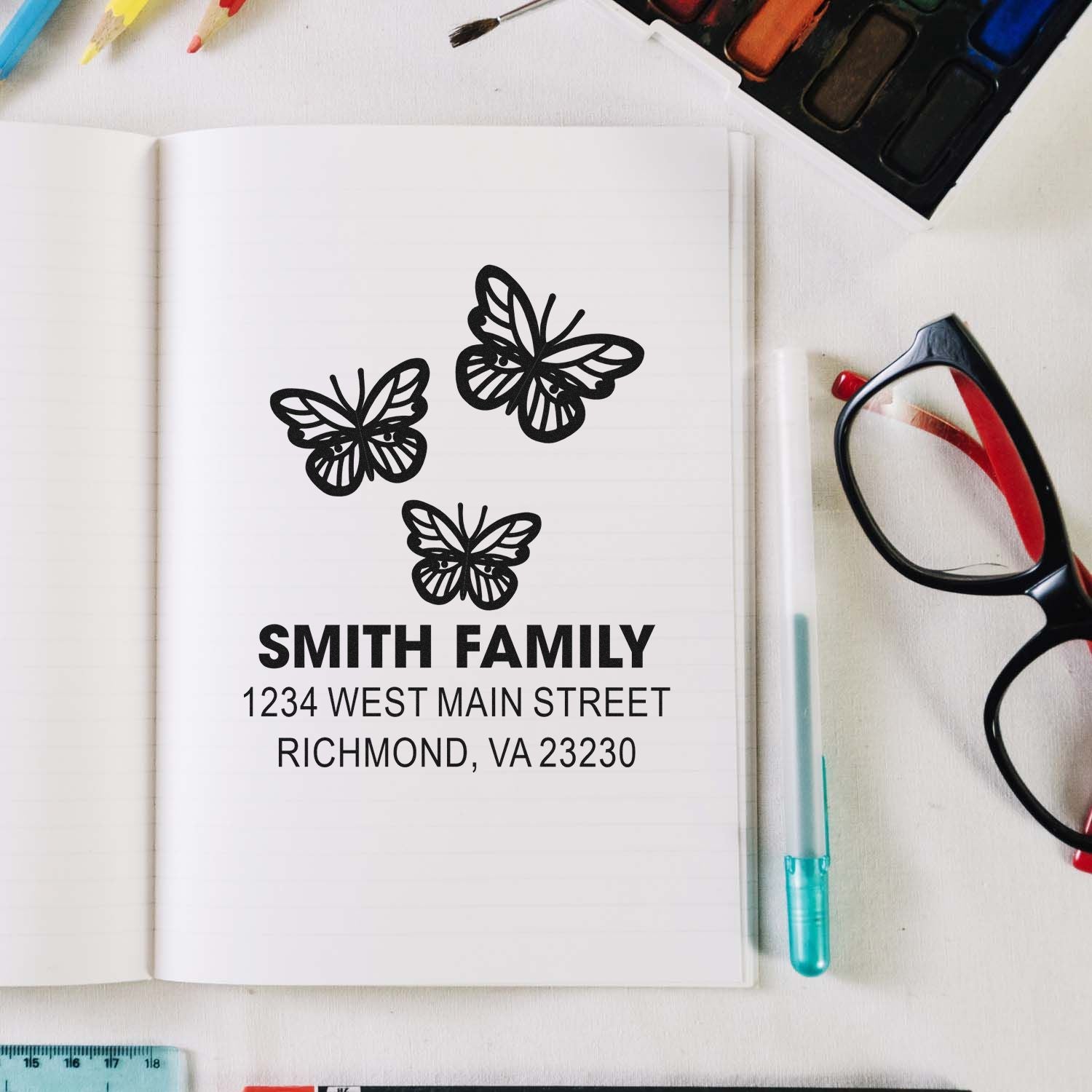 Custom butterfly address rubber stamp for Smith Family, Richmond VA, shown on notebook with art supplies.