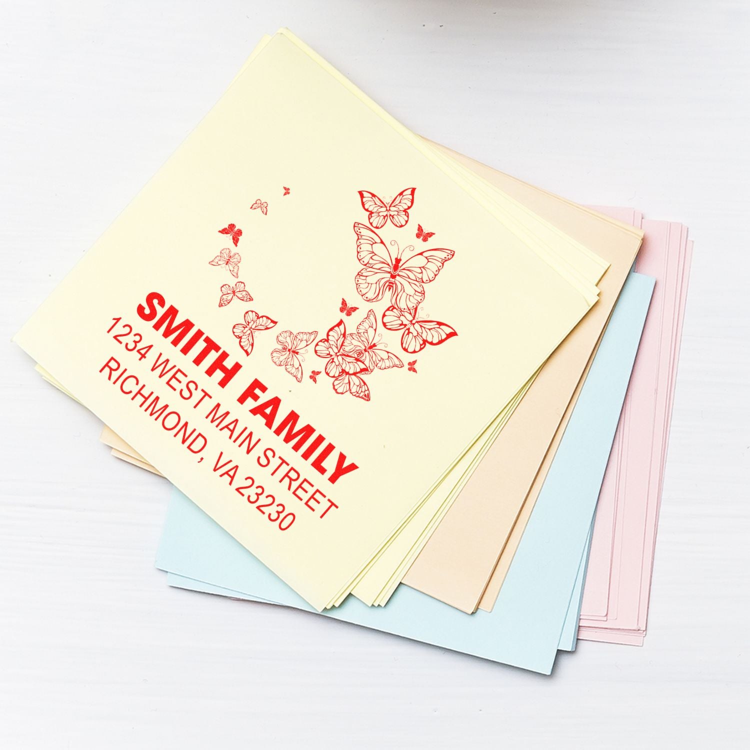 Custom rubber address stamp with butterfly design, showing Smith Family return address on pastel stationery.