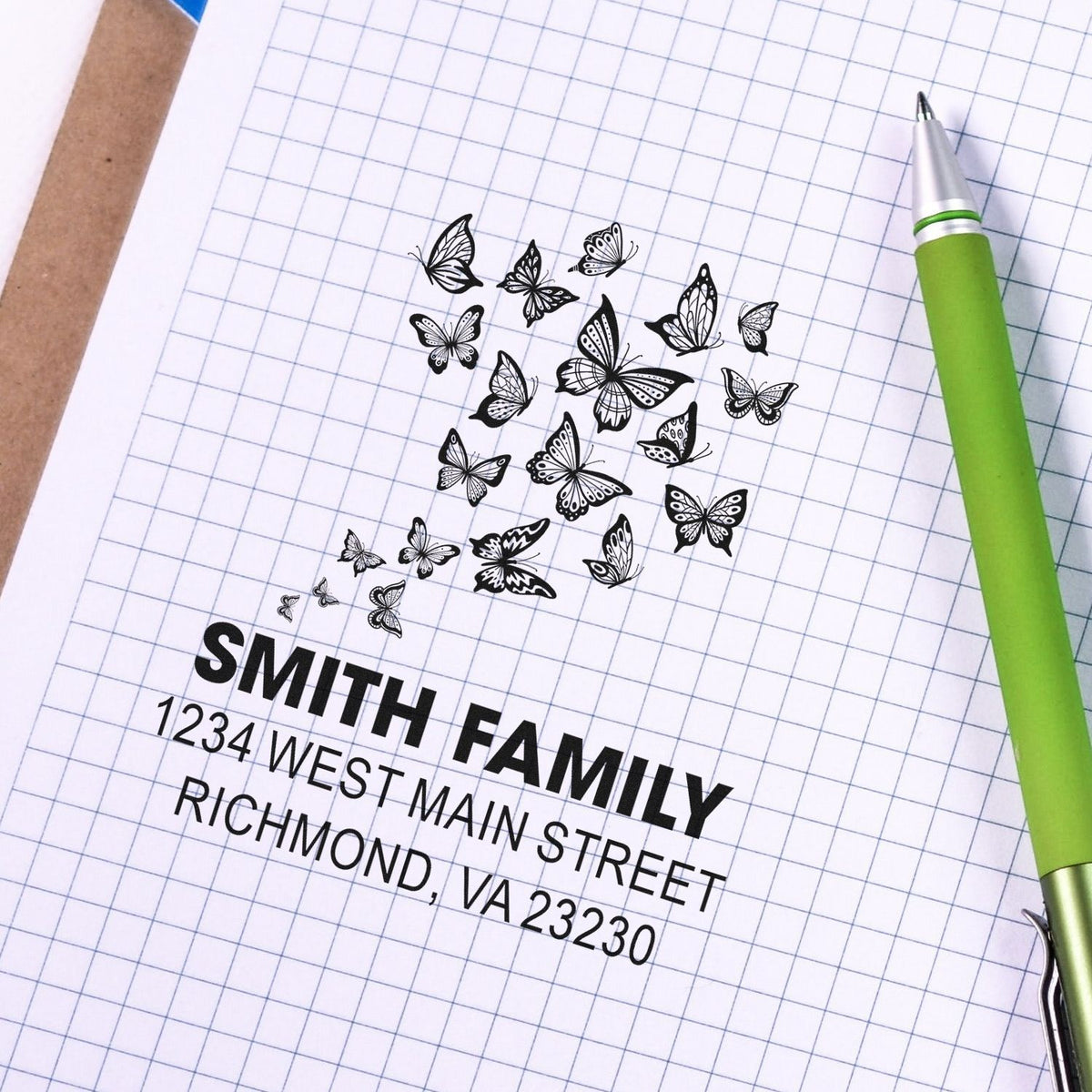 Custom butterfly return address rubber stamp impression on notebook paper, with Smith Family address and green pen.