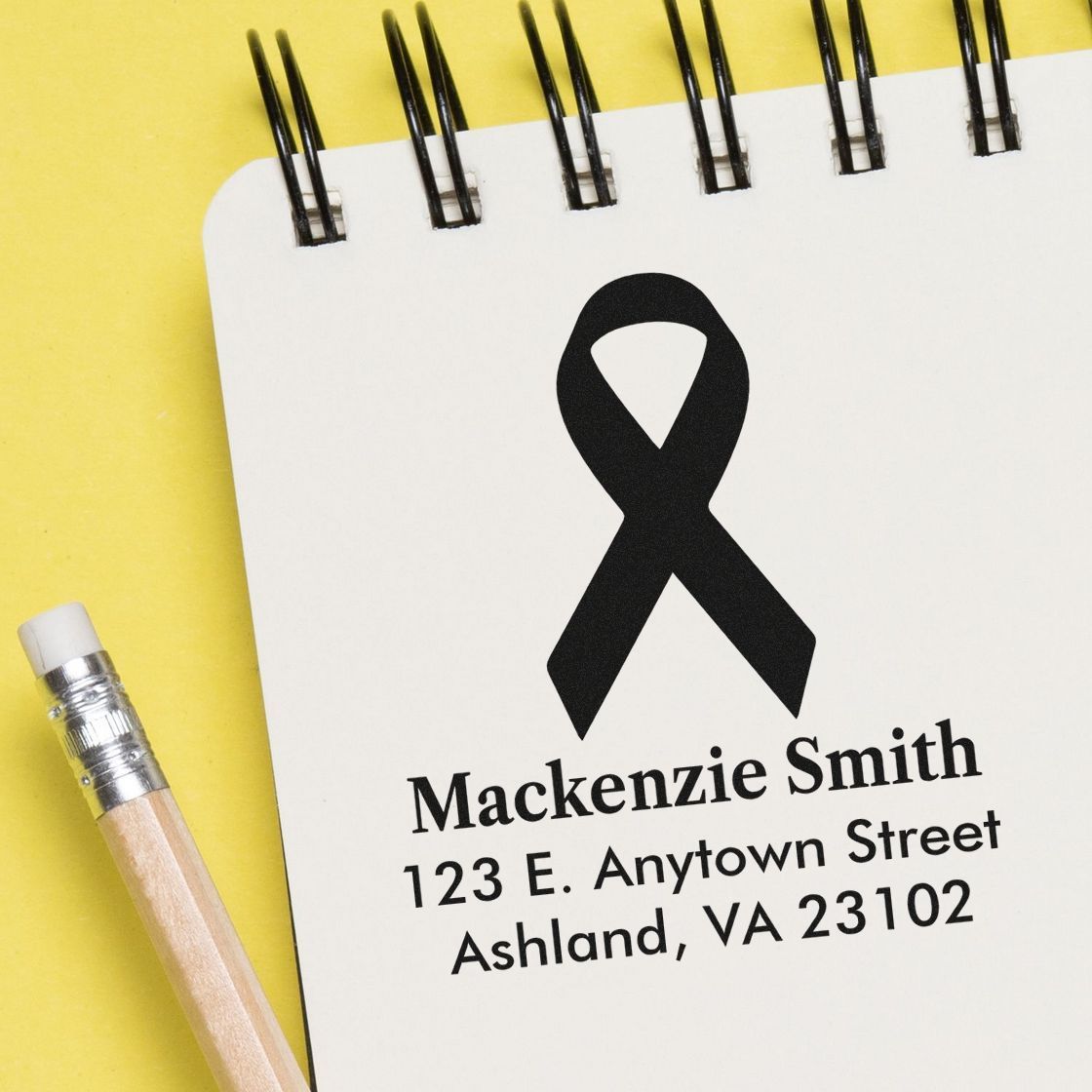 Custom rubber stamp with black awareness ribbon and personalized name and address on notebook page