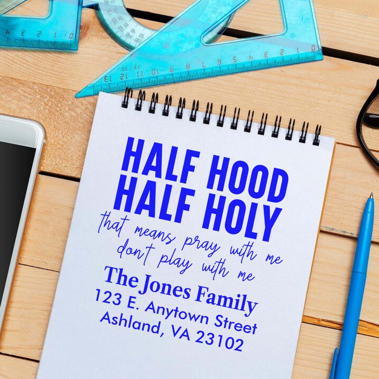 Custom rubber stamp design with Half Hood Half Holy quote, family name, and address on a notebook mockup.