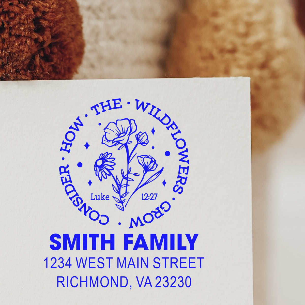 Custom floral return address rubber stamp with family name, Bible verse, and blue ink impression on paper.