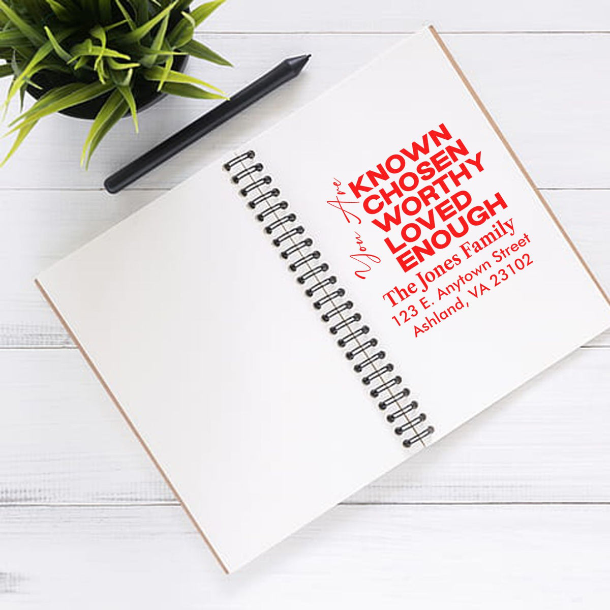 Custom rubber stamp for family return address with inspirational phrase, shown on a notebook page.