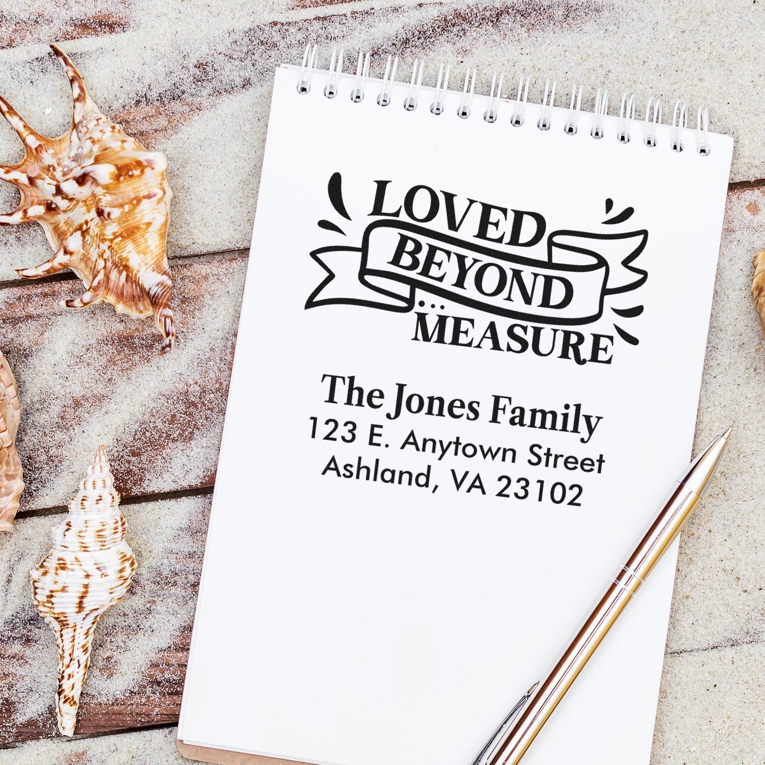 Custom return address rubber stamp with Loved Beyond Measure family design on a notebook, styled with seashells.