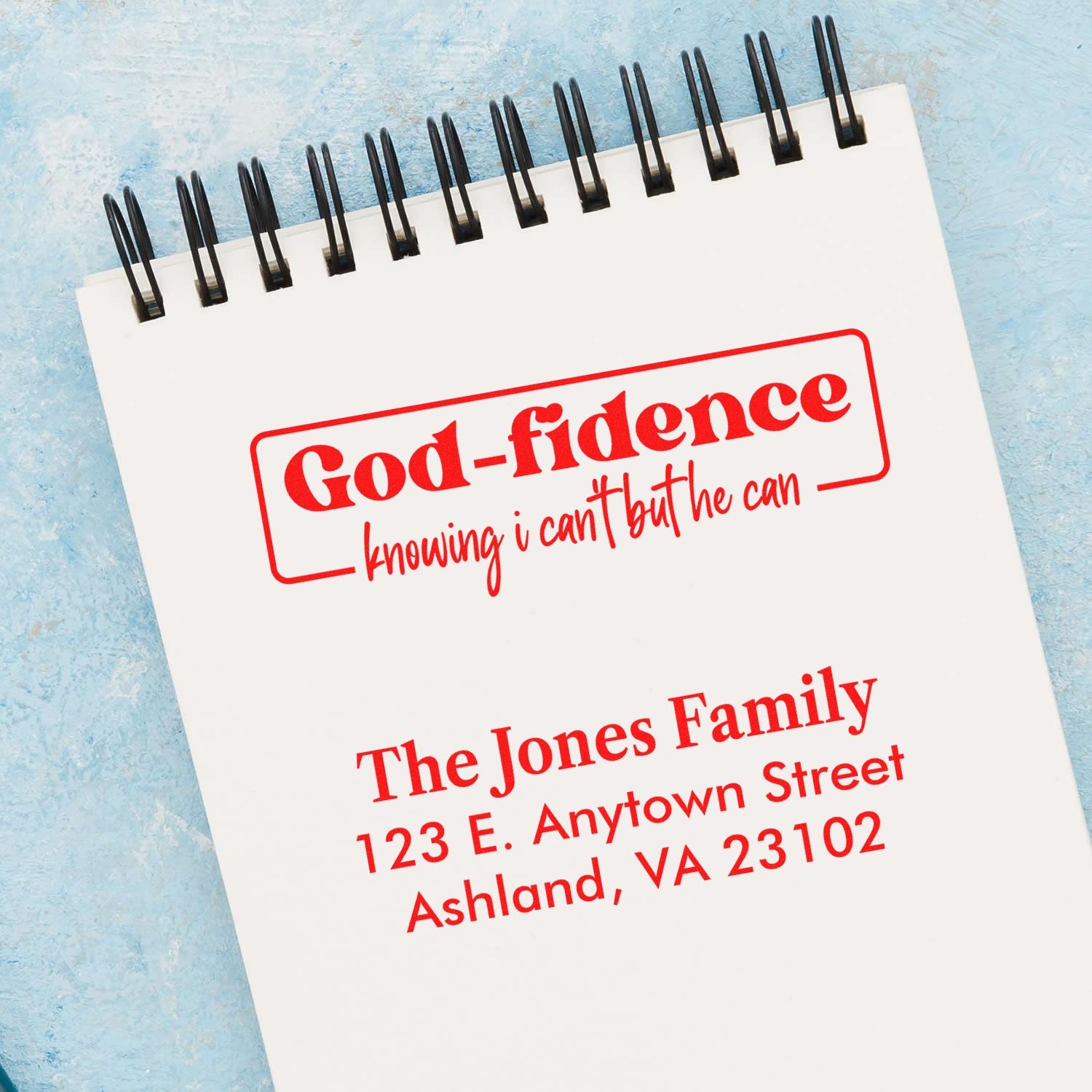 Custom rubber stamps mockup with God-fidence faith quote and personalized return address stamp on a spiral notebook.