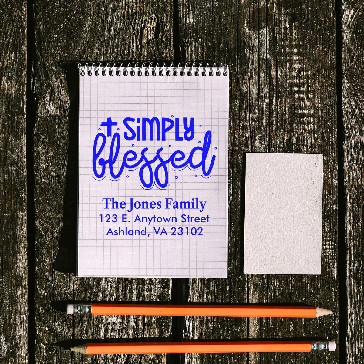 Custom religious return address rubber stamp mockup with Simply Blessed for The Jones Family, blue imprint on notebook.