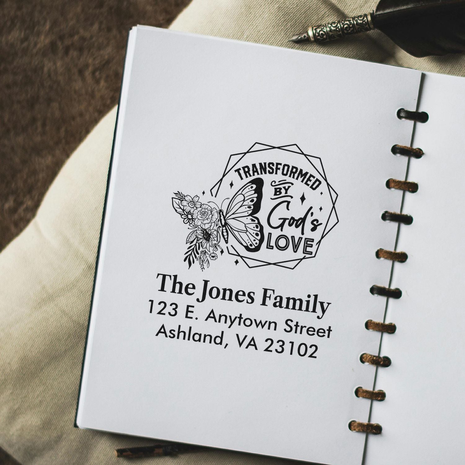 Custom rubber stamp reading Transformed by Gods Love with butterfly floral design and family address on stationery.