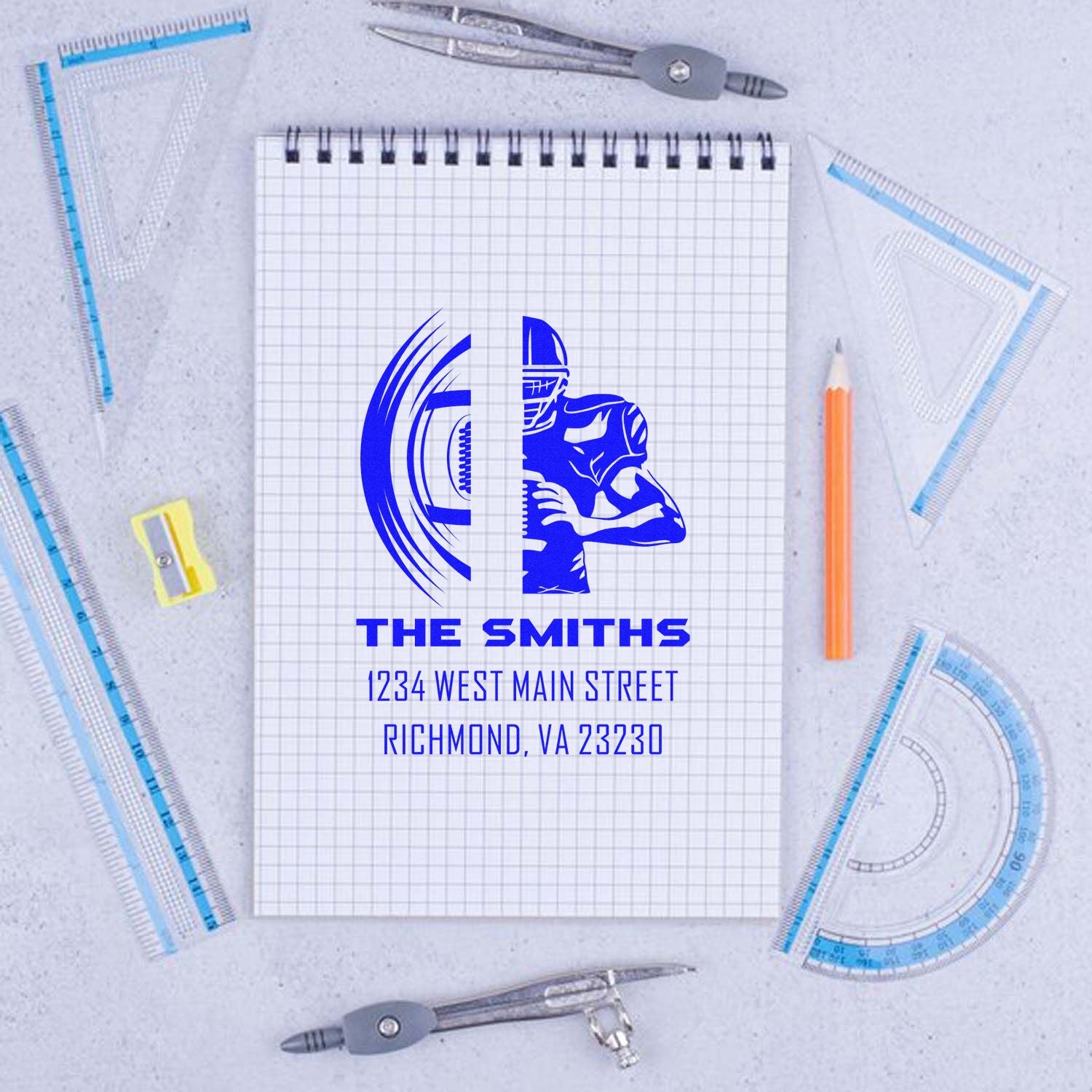 Custom family address rubber stamp with blue logo, name, and address on notebook, styled with drafting tools.