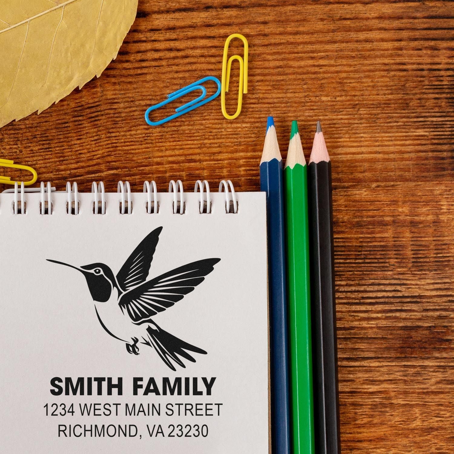 Custom family address rubber stamp with hummingbird logo on notebook, ideal for personalized mailing and stationery.