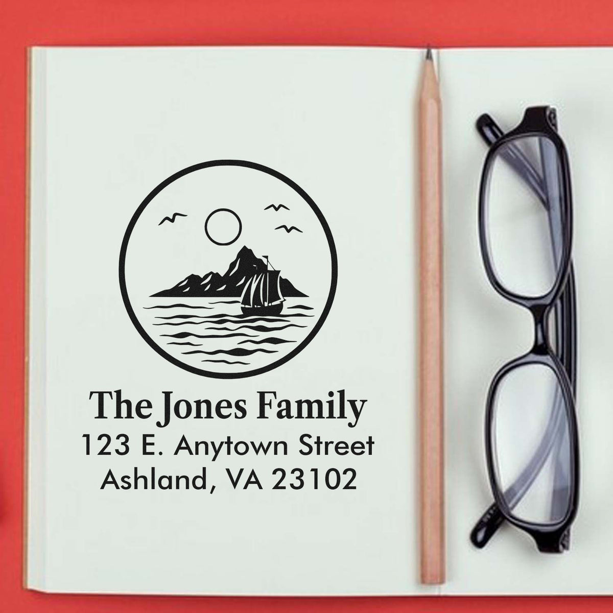 Custom family return address rubber stamp with sailboat logo, shown in a notebook with pencil and eyeglasses.