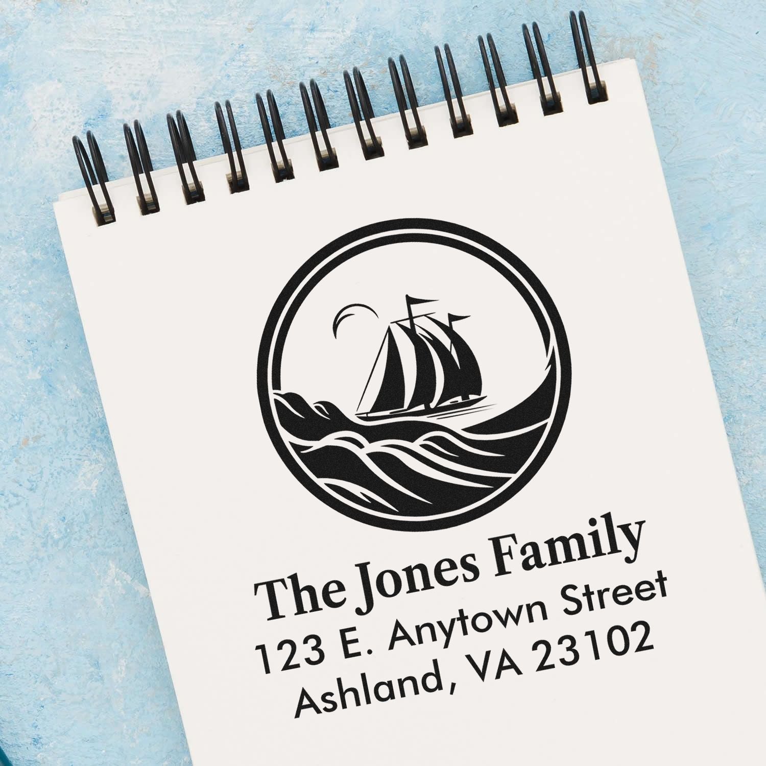 Personalized family address rubber stamp with sailboat logo and return address imprint on a spiral notebook.